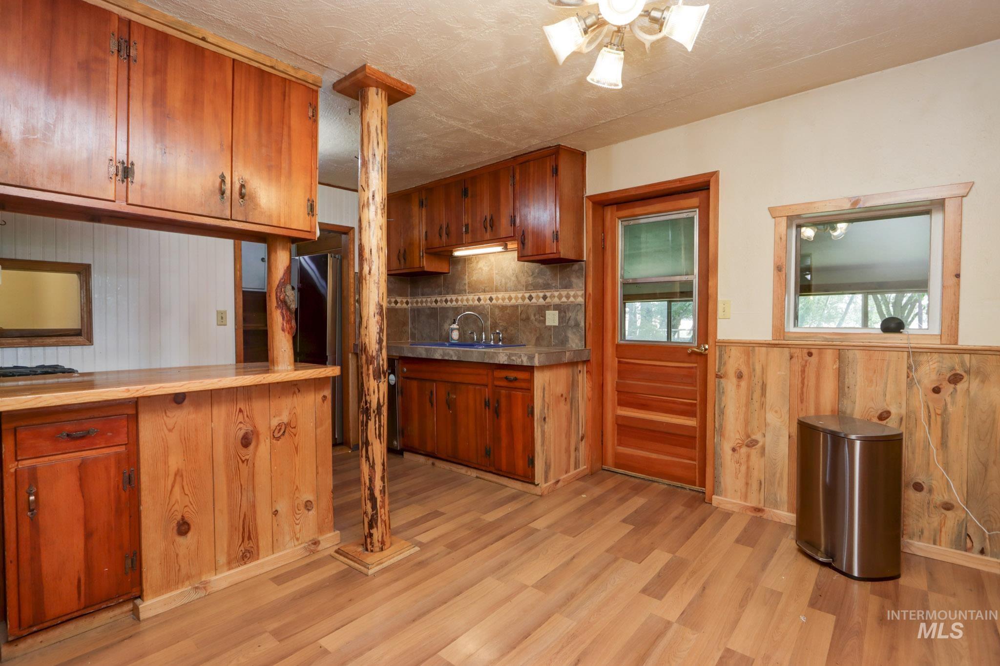 Kitchen featuring wood walls, brown cabinetry, a wainscoted wall, light wood-style floors, and backsplash