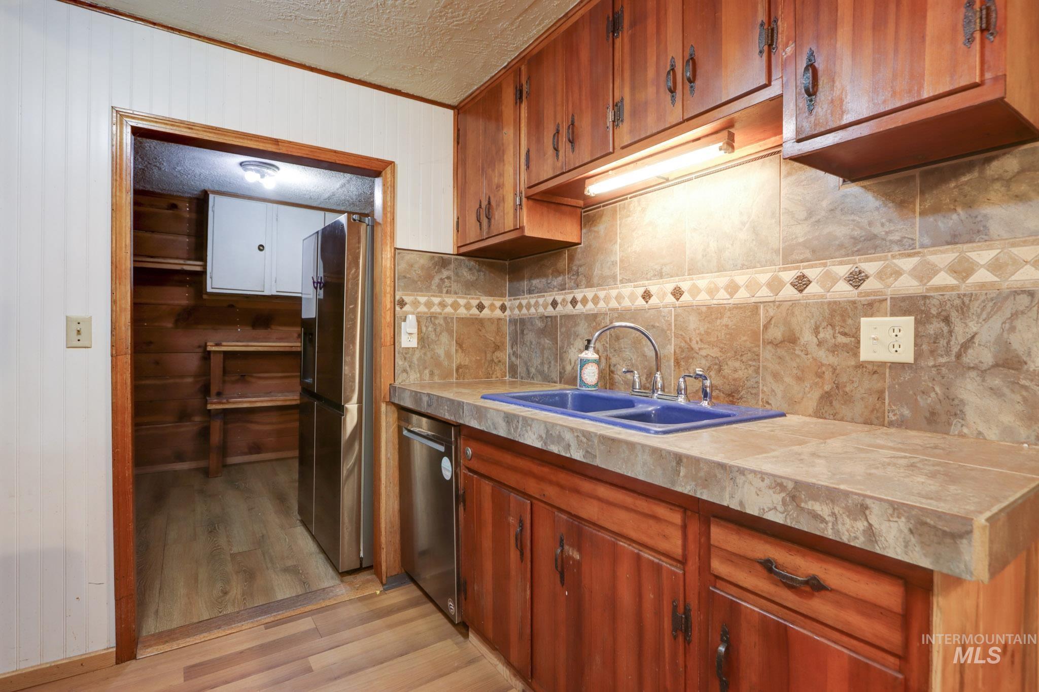 Kitchen with light wood-style floors, wood walls, brown cabinetry, appliances with stainless steel finishes, and ornamental molding