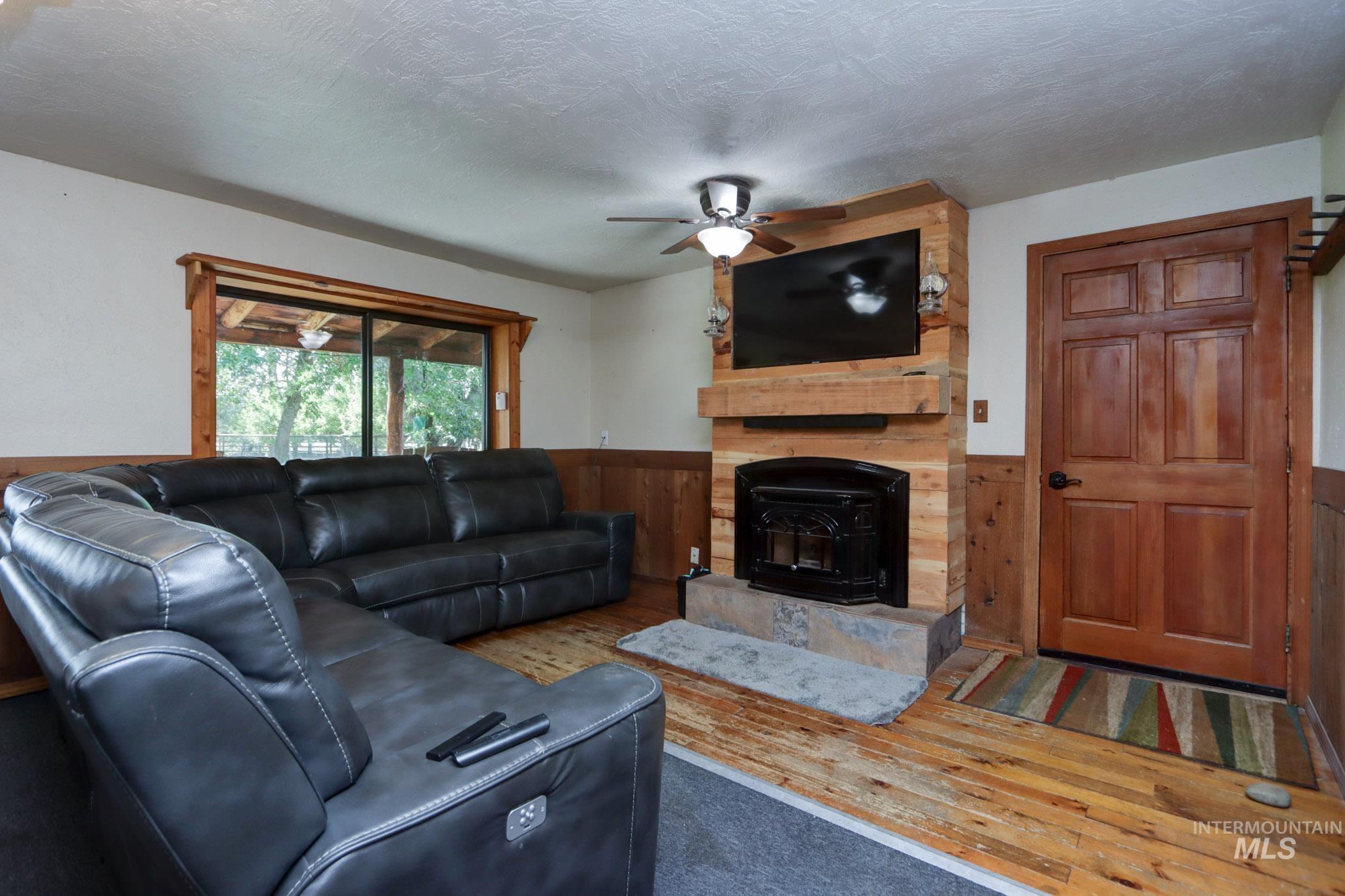 Living area with wood-type flooring, a wainscoted wall, wooden walls, a textured ceiling, and a wood stove