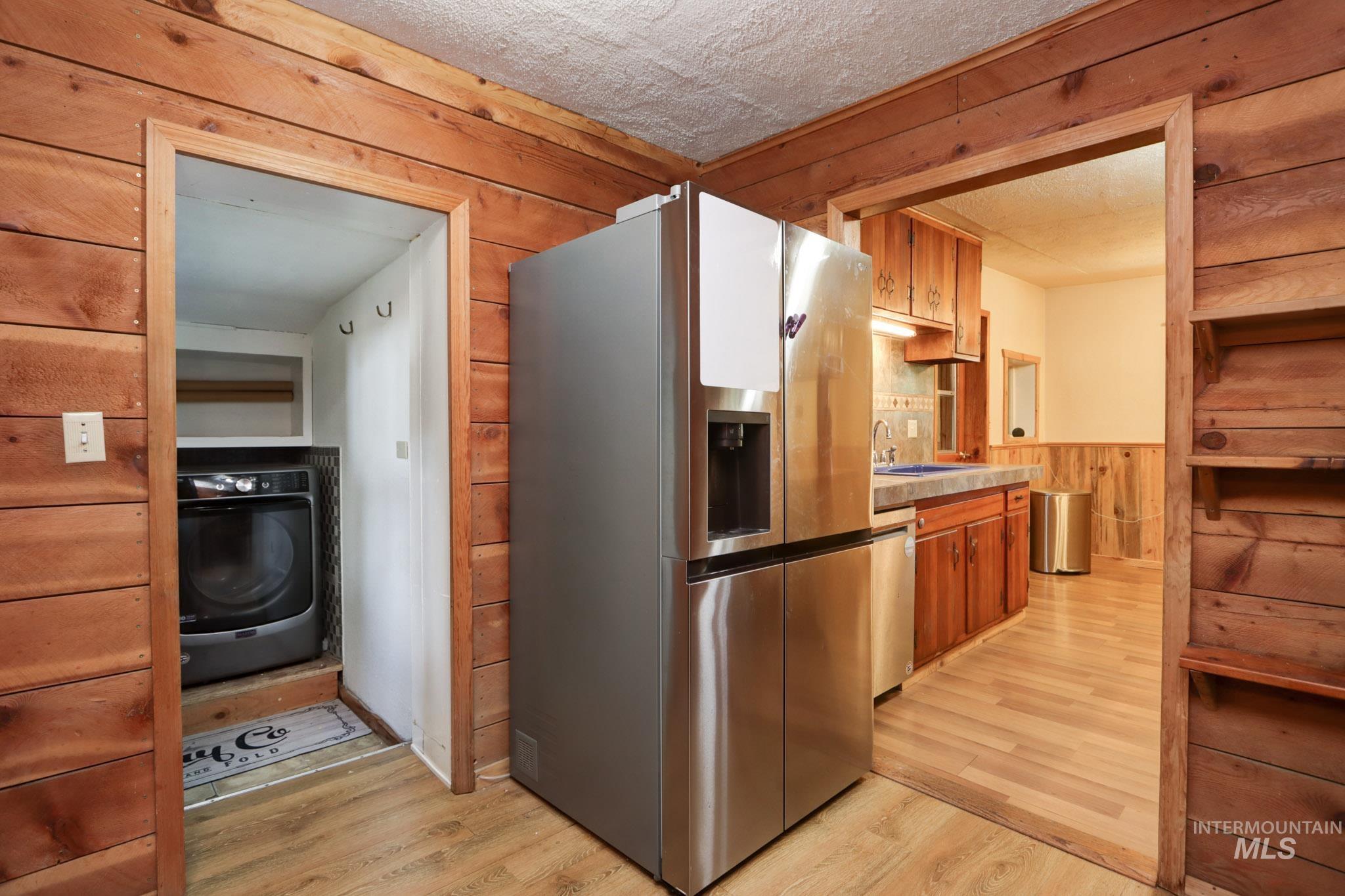 Kitchen featuring wooden walls, brown cabinets, appliances with stainless steel finishes, washer / dryer, and light wood-style flooring