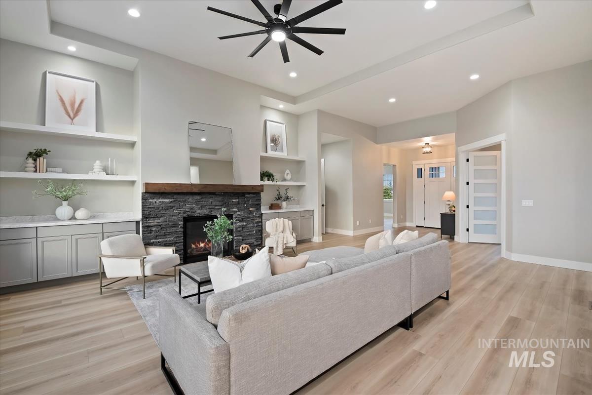 Living room with built in features, a fireplace, a ceiling fan, recessed lighting, and light wood finished floors
