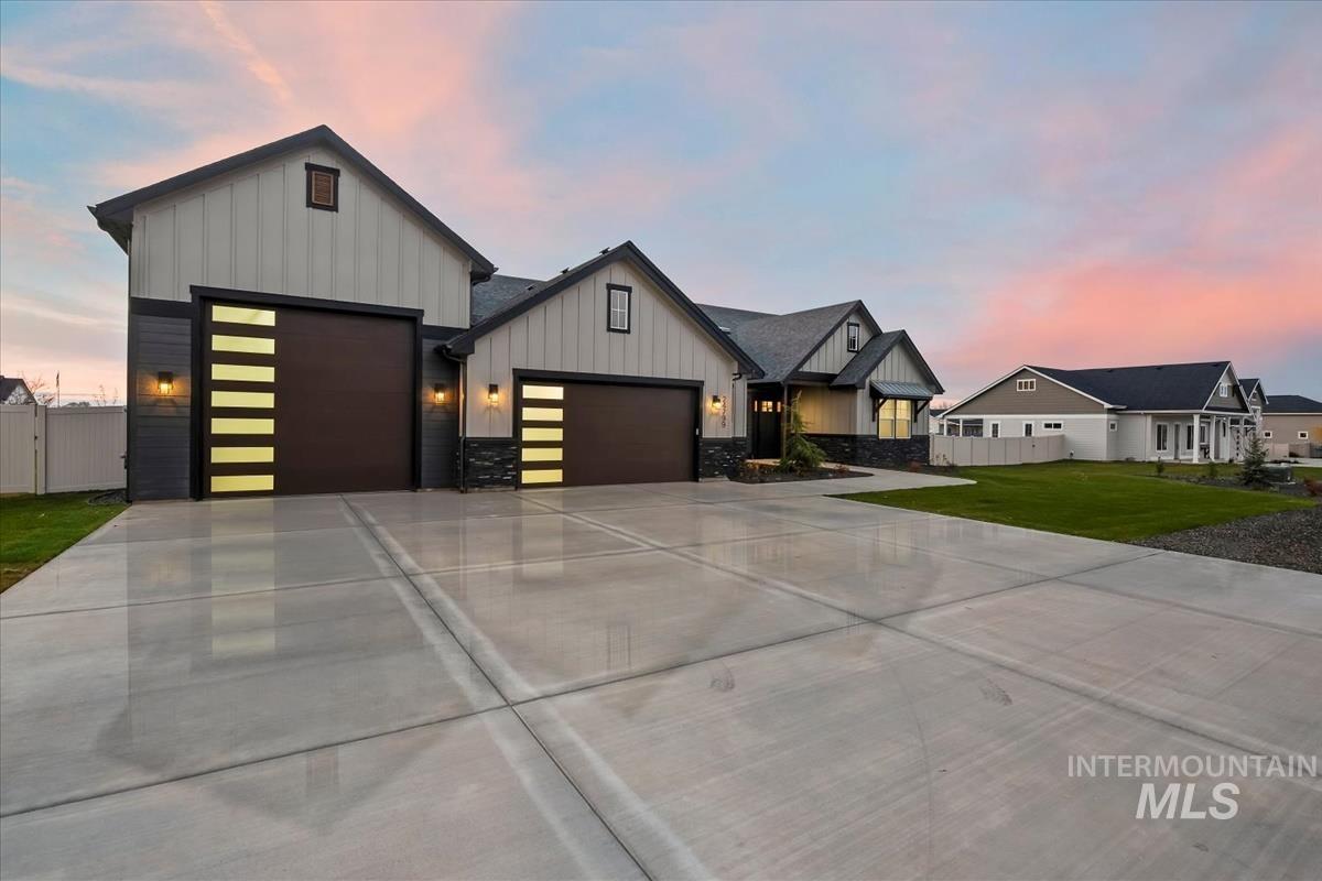 Modern farmhouse style home with board and batten siding, an attached garage, driveway, and stone siding