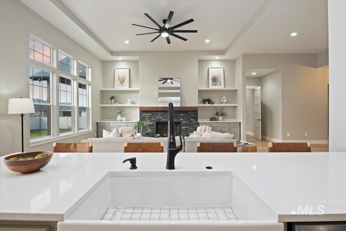Kitchen view of built in shelves, ceiling fan, recessed lighting, a fireplace, and light stone counters