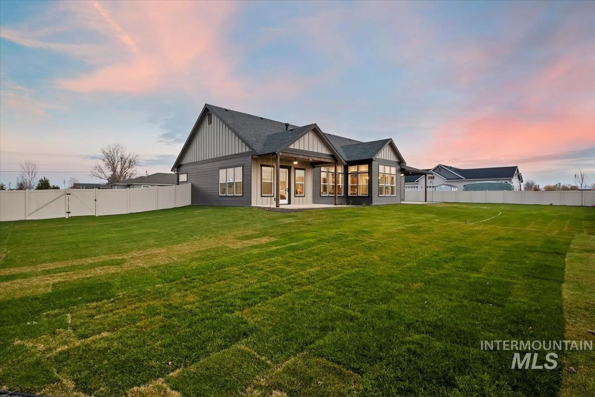 Back of property at dusk with a fenced backyard, board and batten siding, a patio, and roof with shingles