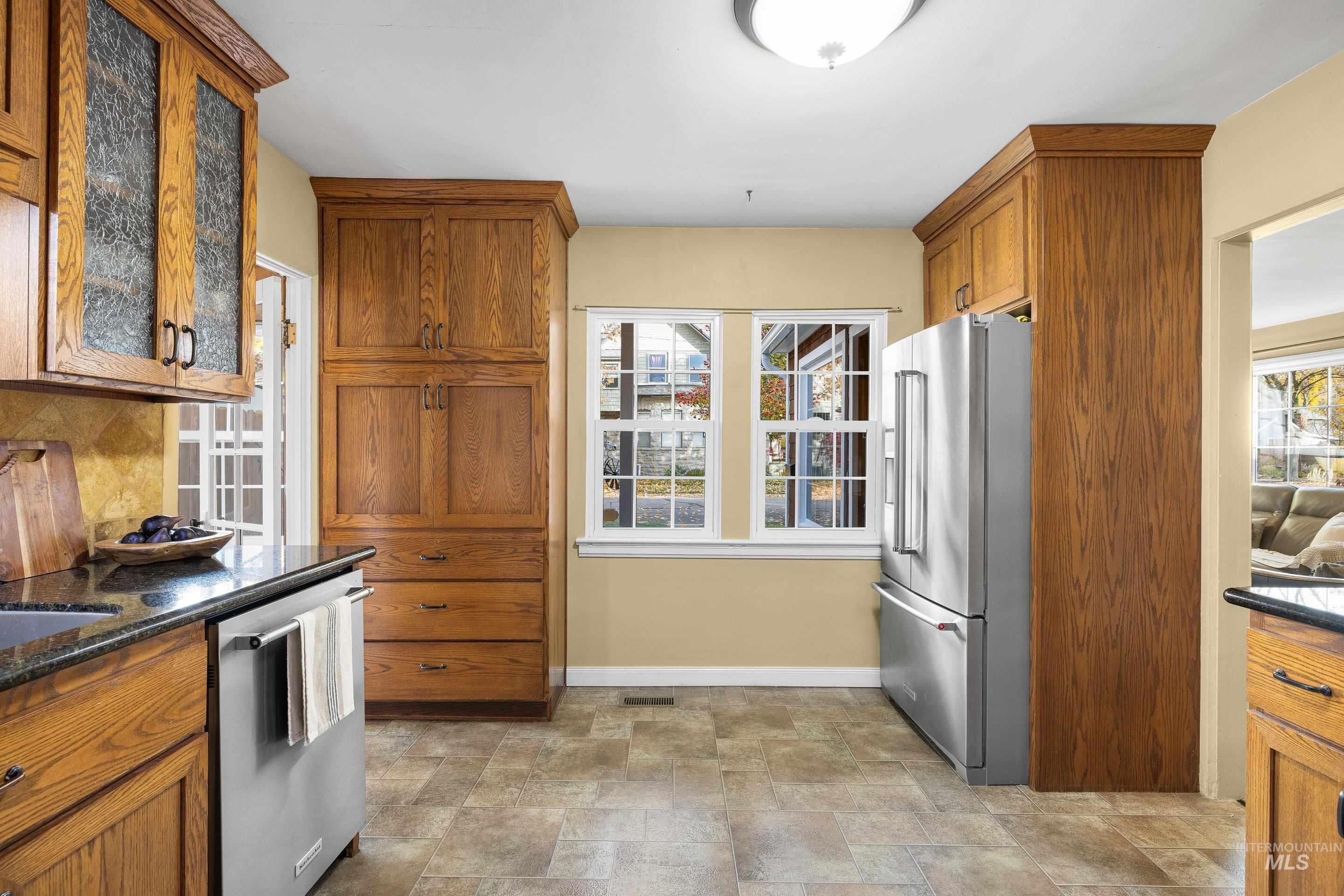 Kitchen featuring brown cabinetry, stainless steel appliances, stone finish floors, dark stone counters, and tasteful backsplash