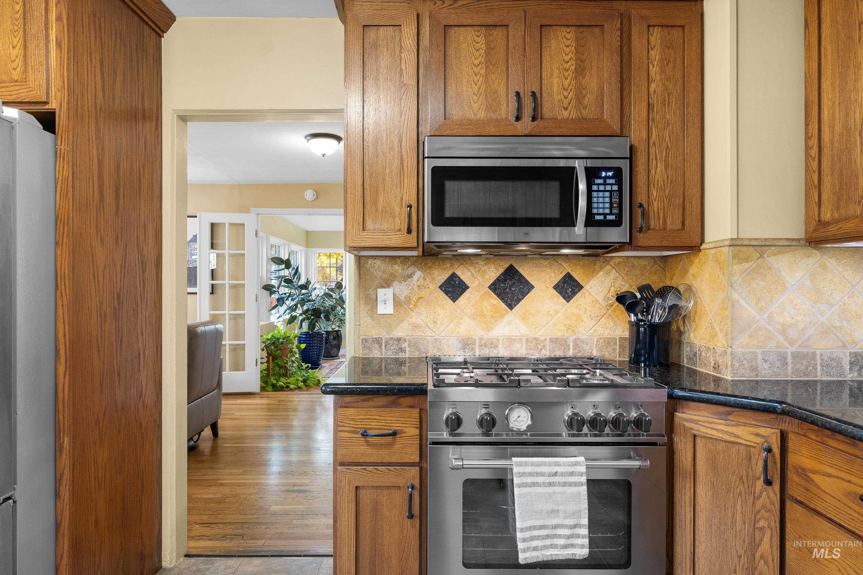 Kitchen featuring brown cabinetry, stainless steel appliances, backsplash, and dark stone countertops