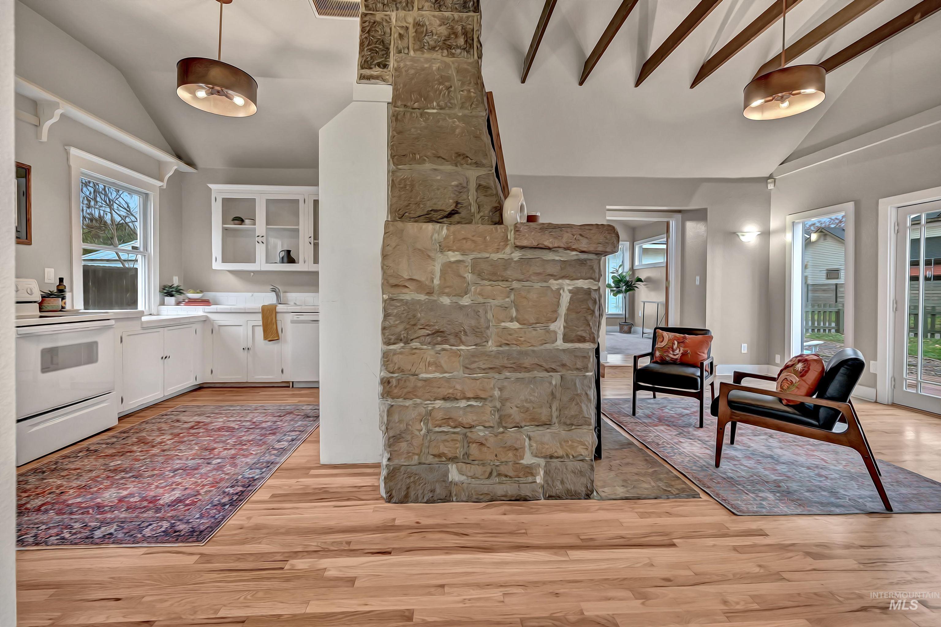 Open, light-filled layout highlighting the stone fireplace, airy kitchen, and vaulted ceiling with exposed beams.