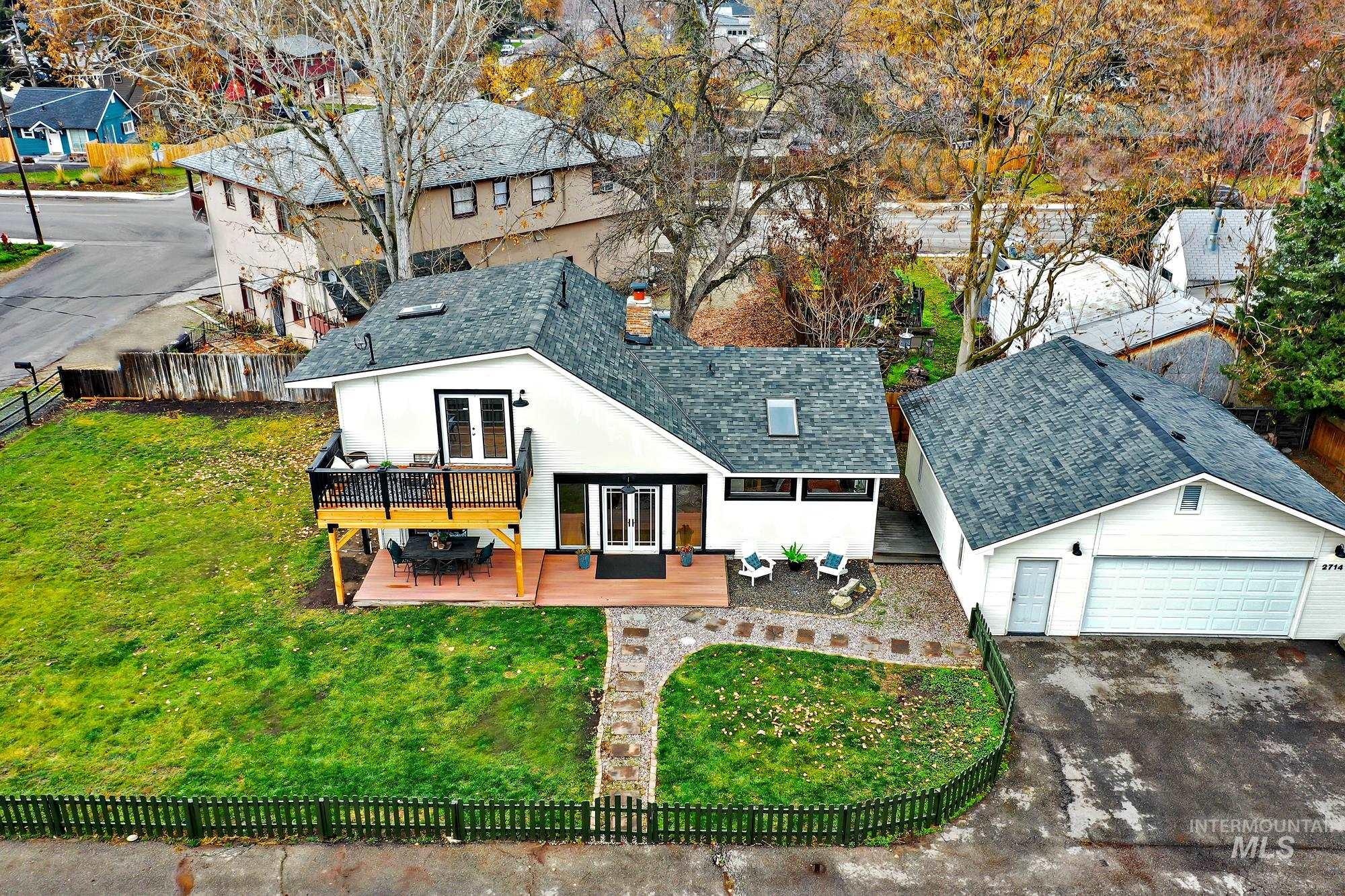 Bird?s-eye perspective highlighting the home?s outdoor living spaces, including the upper deck, ground-level patio, and generous yard enclosed by a picket fence.