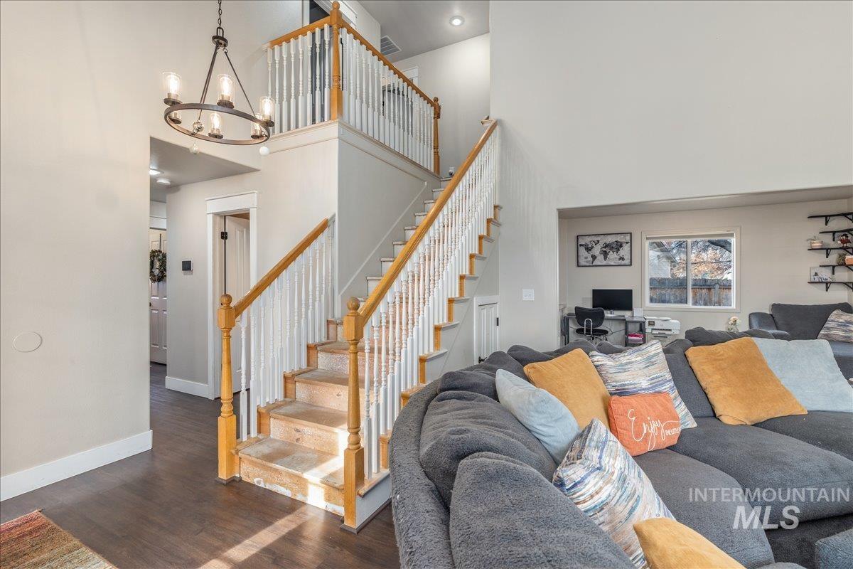 Living area with dark wood-type flooring, a high ceiling, an office area, stairs, and a chandelier