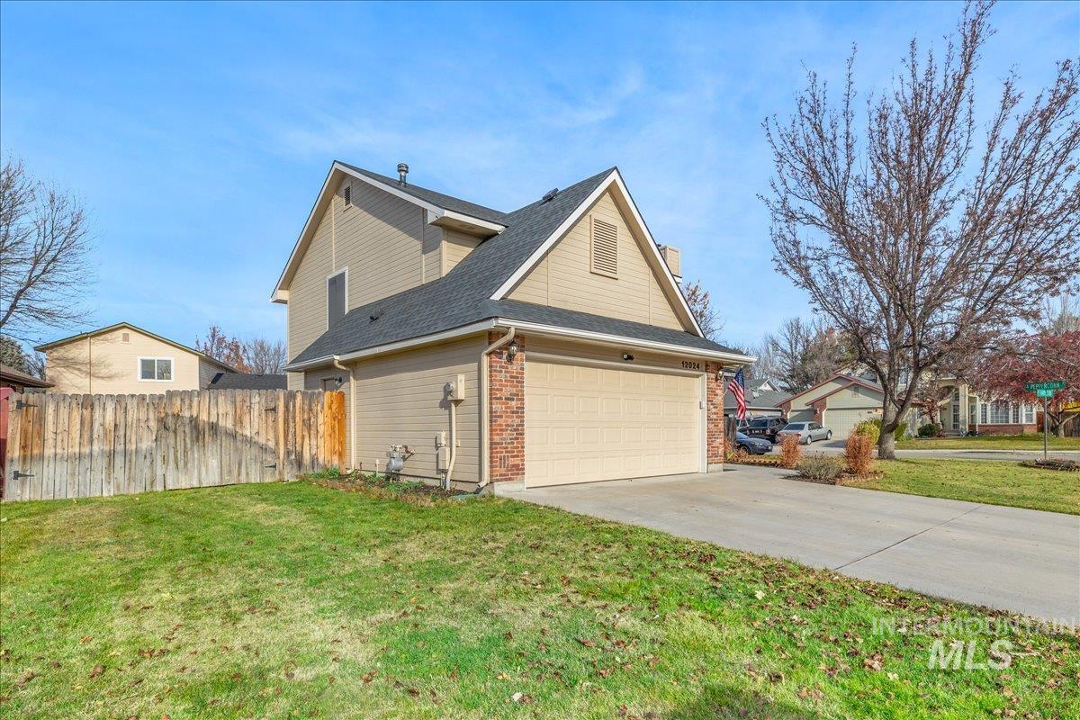 View of side of property with driveway, a shingled roof, brick siding, a garage, and a chimney