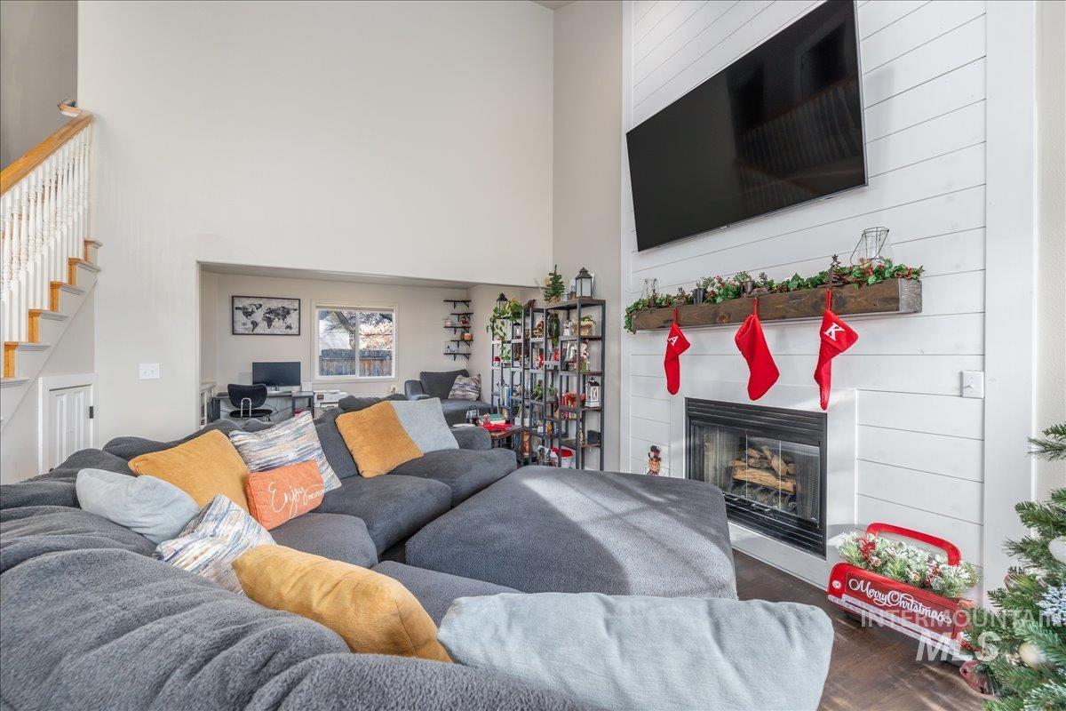 Living room with a glass covered fireplace, dark wood finished floors, a towering ceiling, and a desk