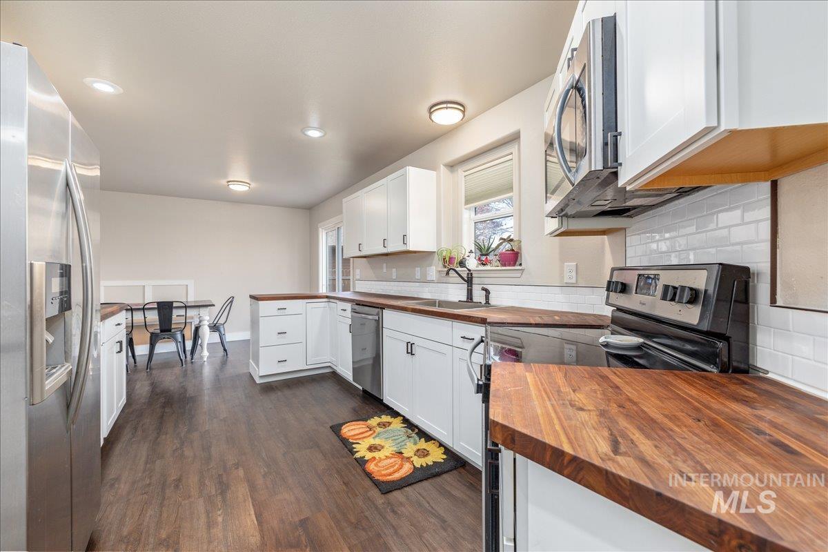Kitchen featuring appliances with stainless steel finishes, white cabinetry, dark wood-style floors, butcher block countertops, and backsplash
