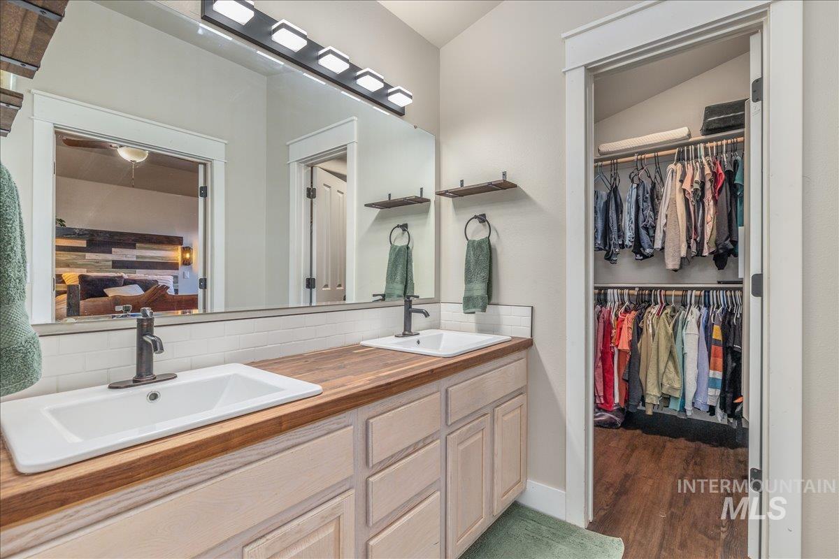Ensuite bathroom featuring double vanity, backsplash, dark wood finished floors, and a walk in closet
