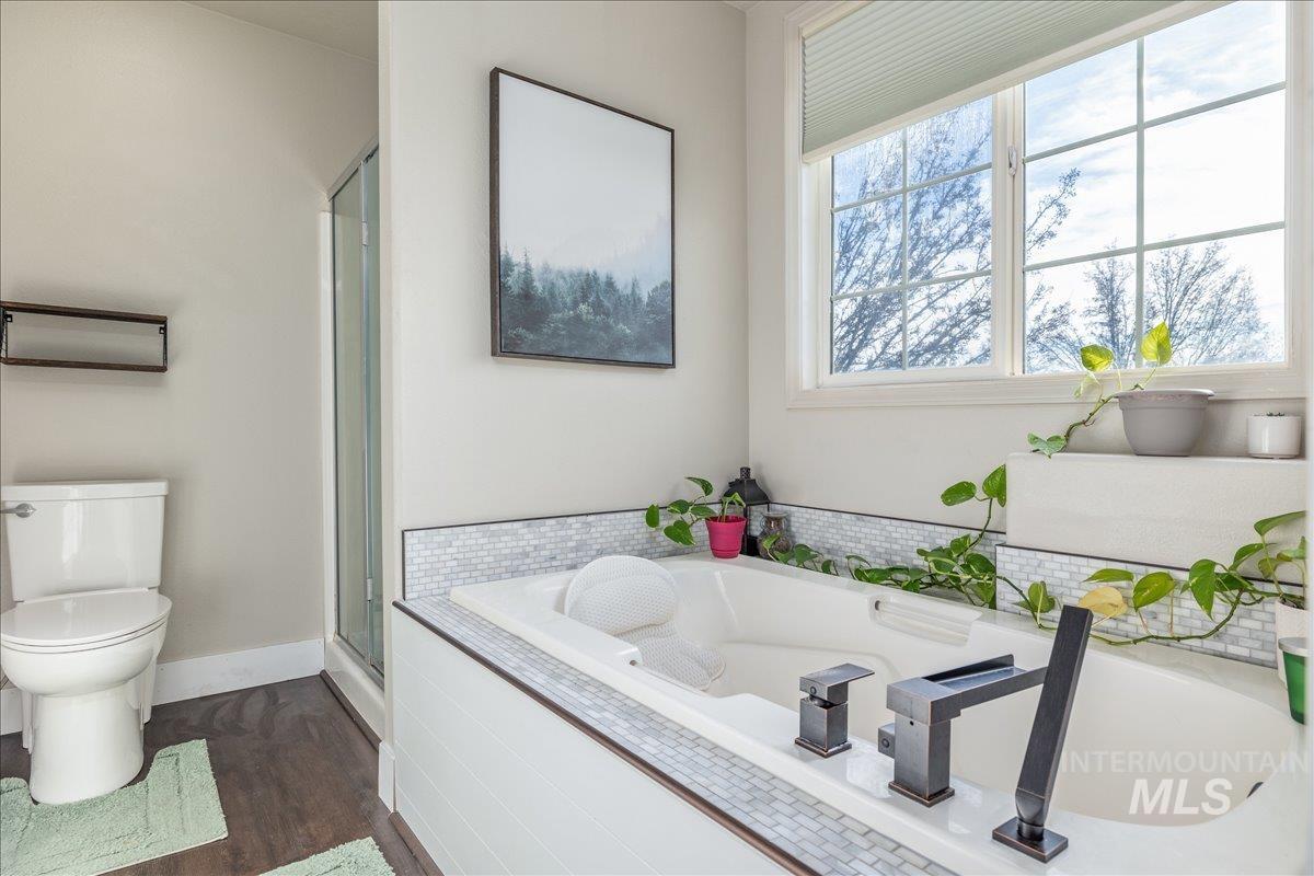 Full bath featuring a stall shower, a garden tub, and dark wood-type flooring