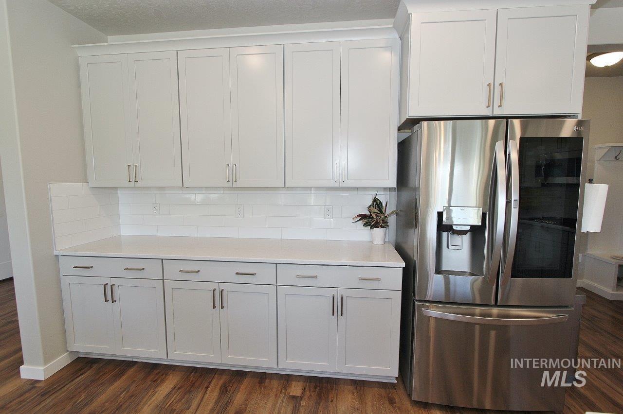 Kitchen featuring stainless steel fridge, tasteful backsplash, dark wood-style floors, and white cabinetry
