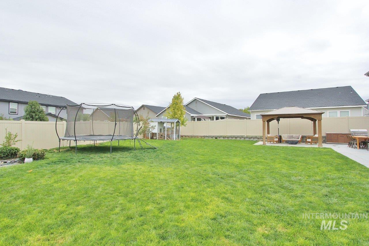 Fenced backyard featuring a trampoline, a gazebo, and a patio
