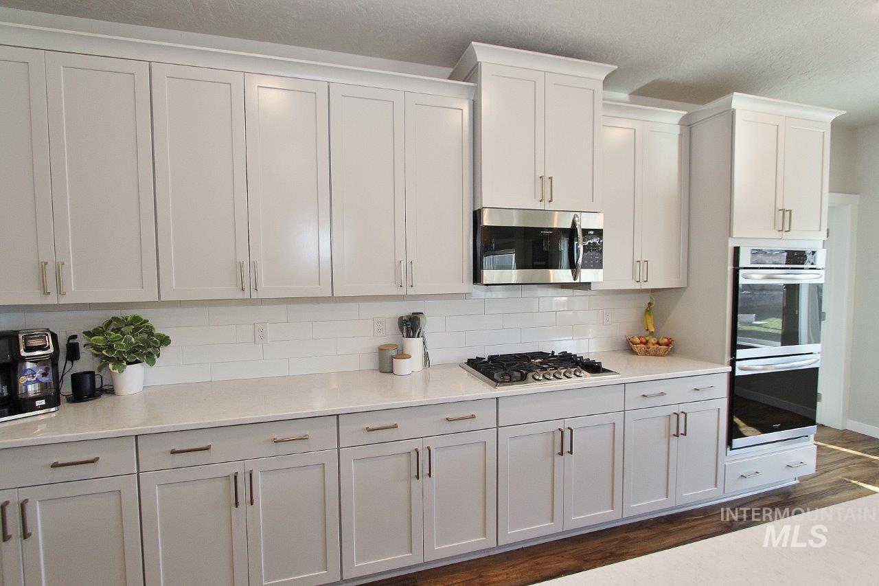 Kitchen featuring backsplash, stainless steel appliances, light stone counters, dark wood-style flooring, and white cabinets