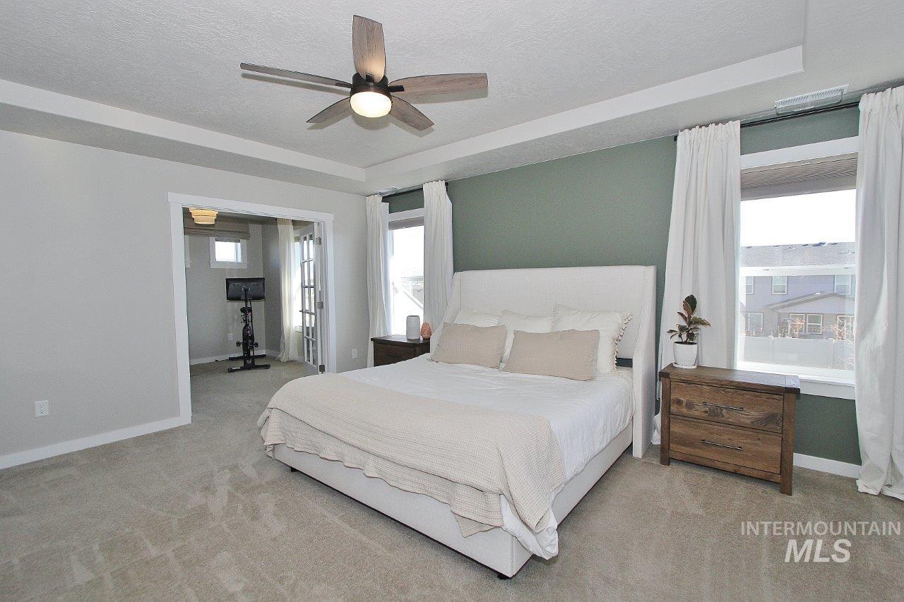 Bedroom with a tray ceiling, a textured ceiling, a ceiling fan, and light colored carpet