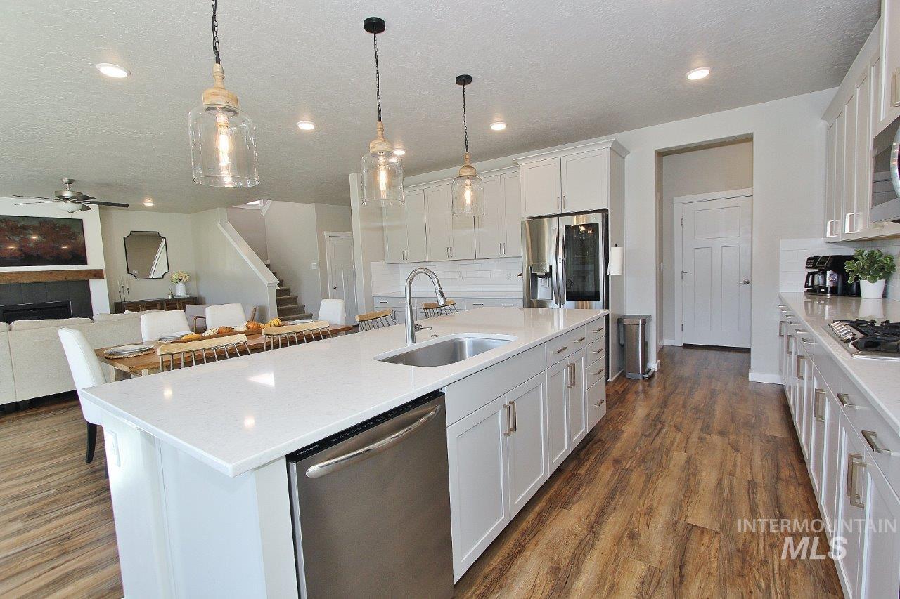 Kitchen featuring white cabinets, stainless steel appliances, a fireplace, a center island with sink, and pendant lighting