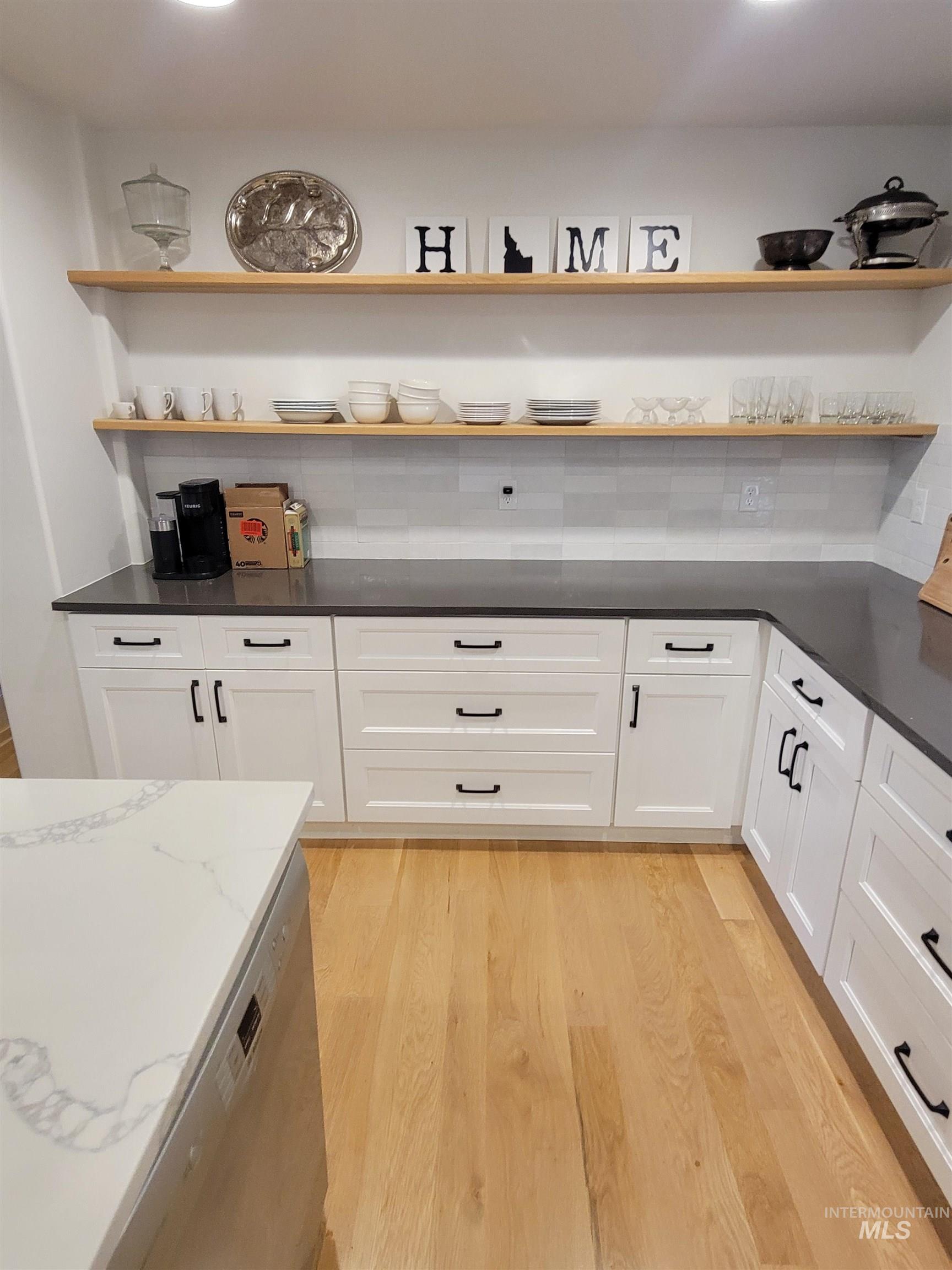 Kitchen with open shelves, light wood-type flooring, dark stone countertops, dishwasher, and white cabinetry