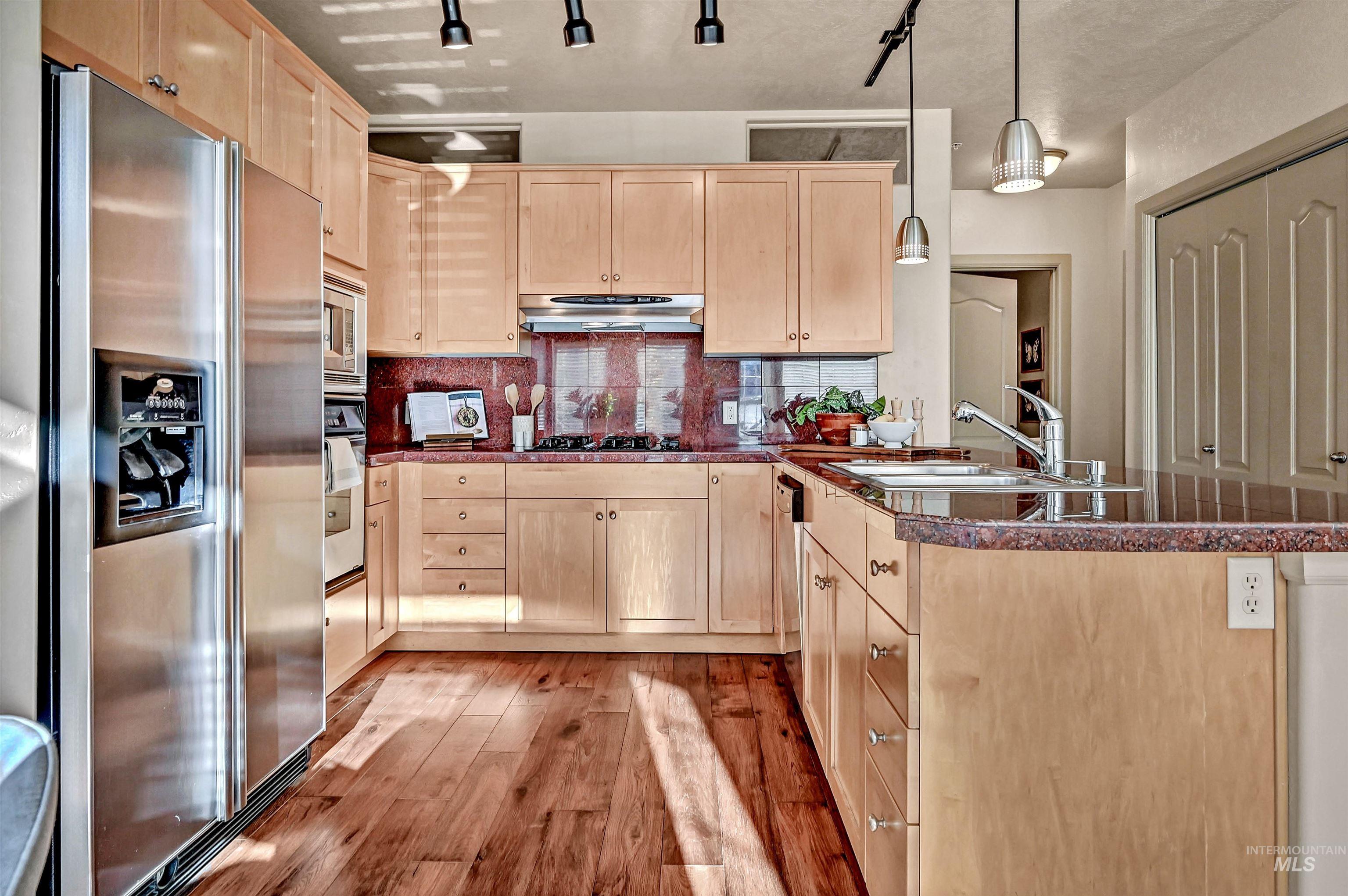 Kitchen with stainless steel appliances, maple cabinetry, light wood-style floors, new light fixtures, and granite surfaces.