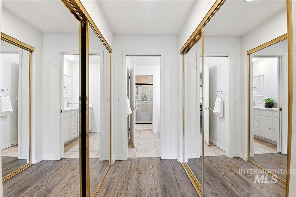 Hallway featuring wood-finish flooring, mirrored closet doors with gold-tone frames, and white walls