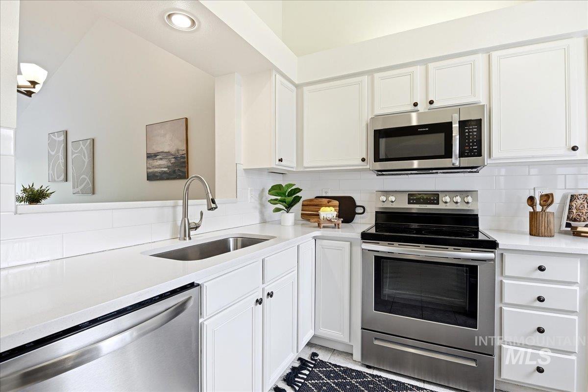 Kitchen featuring white cabinetry, stainless steel appliances, a subway tile backsplash, solid surface countertops, and a stainless steel sink with a gooseneck faucet