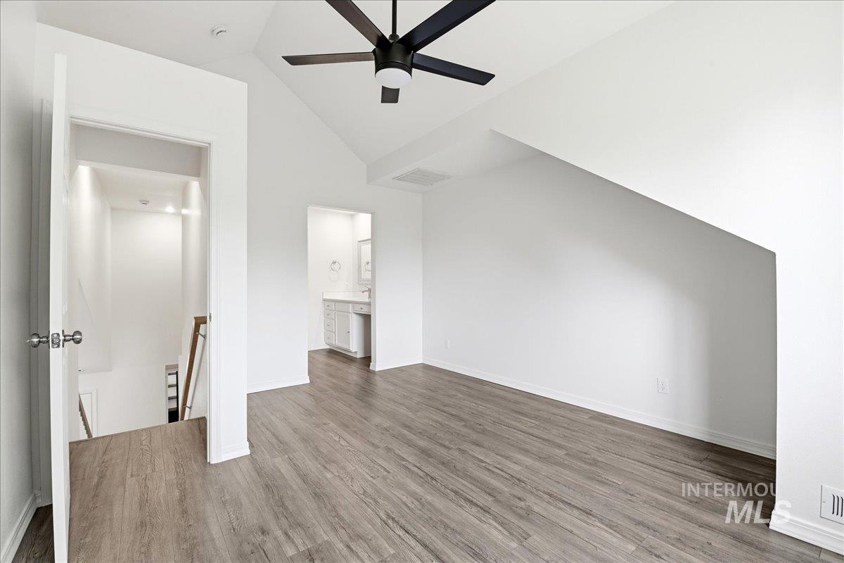Spacious room featuring vaulted ceilings, wood-finish flooring, a contemporary ceiling fan, and access to a full bathroom with a vanity and mirror