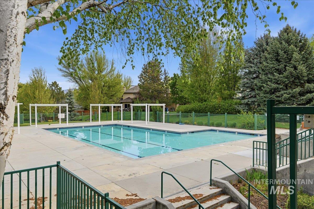 Outdoor swimming pool with concrete decking, surrounded by a green perimeter fence and mature trees