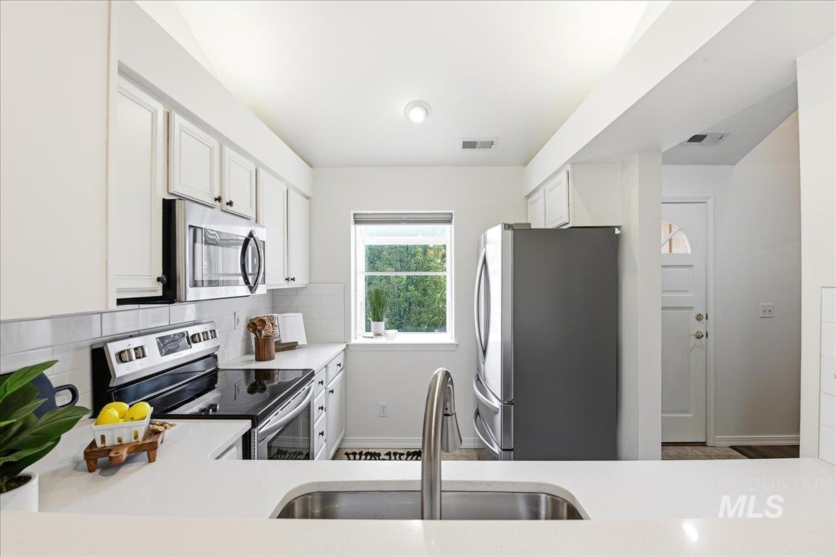 Modern kitchen featuring white cabinetry, stainless steel appliances, a tile backsplash, light-toned countertops, and a window above the sink