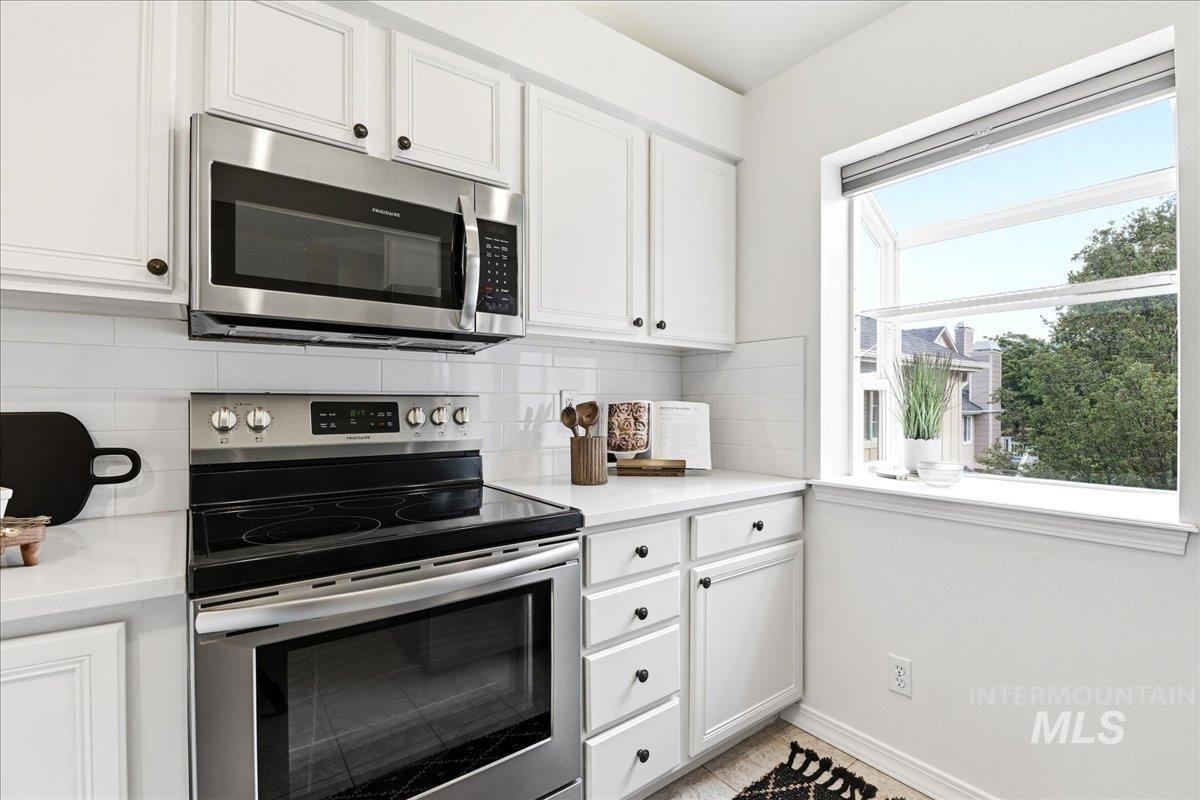 Modern kitchen showcasing white shaker cabinetry with dark hardware, stainless steel appliances including a range and microwave, white subway tile backsplash, and a large window