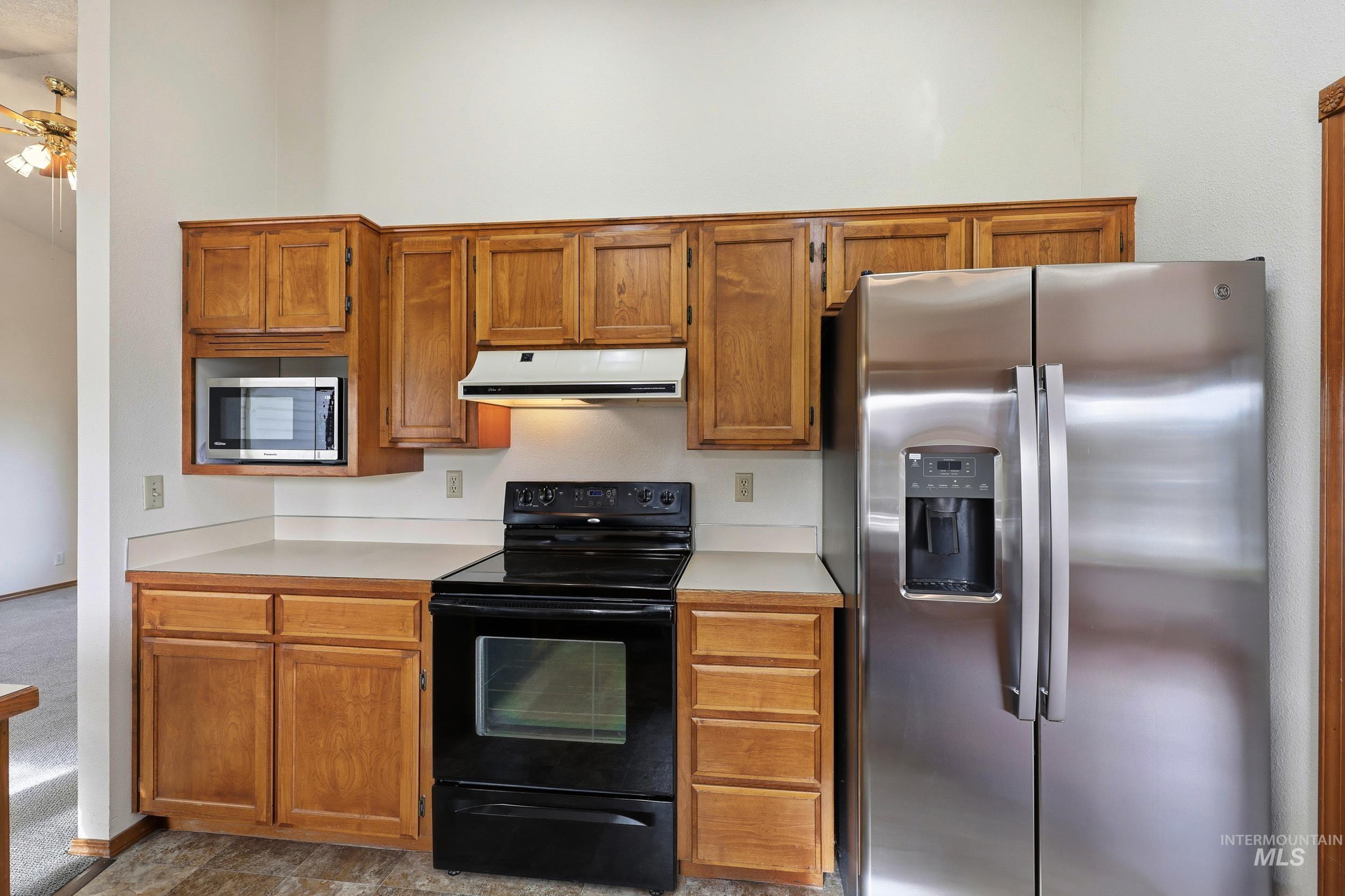 Kitchen featuring appliances with stainless steel finishes, light countertops, brown cabinetry, extractor fan, and ceiling fan