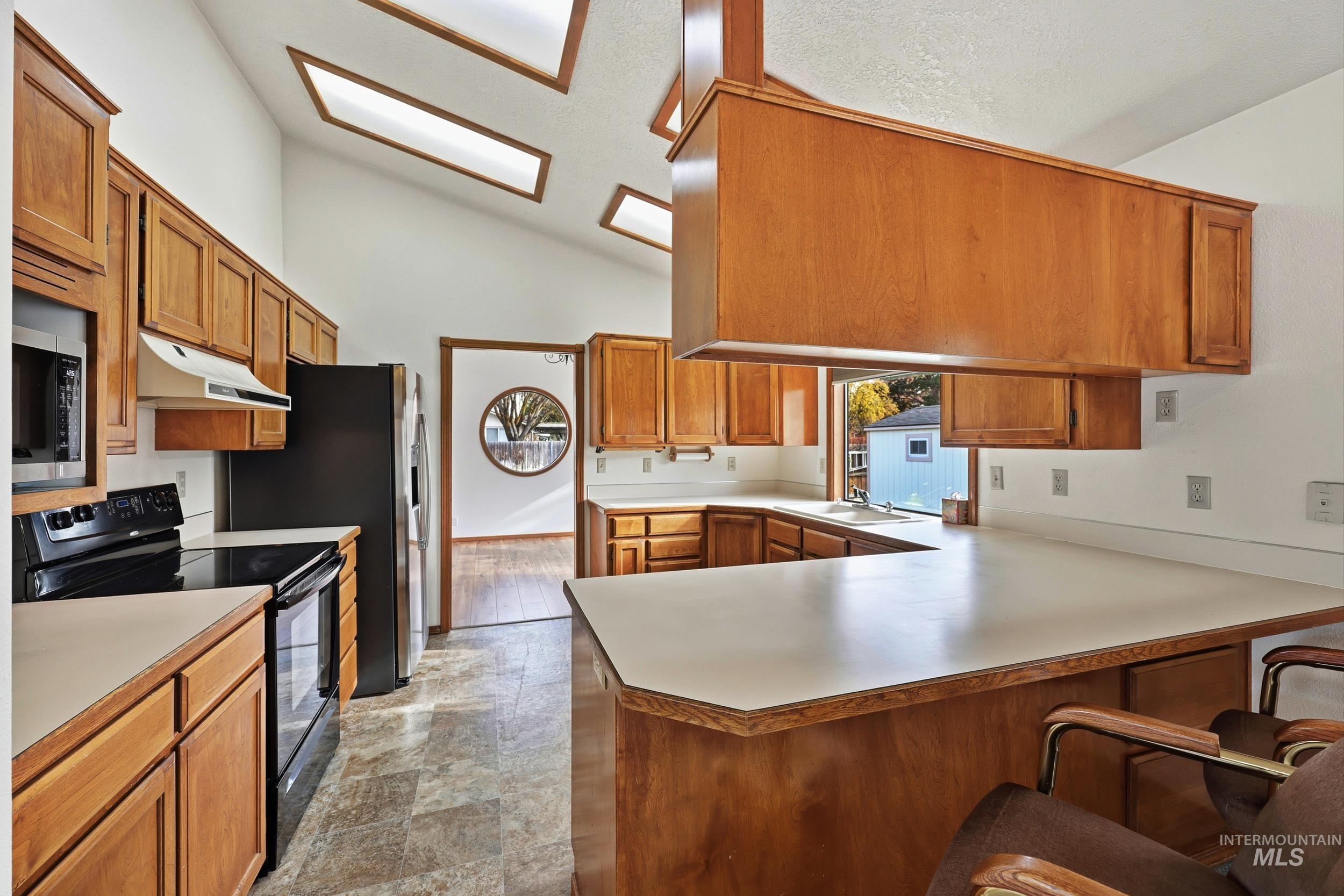 Kitchen with black electric range, brown cabinetry, light countertops, lofted ceiling, and a kitchen bar