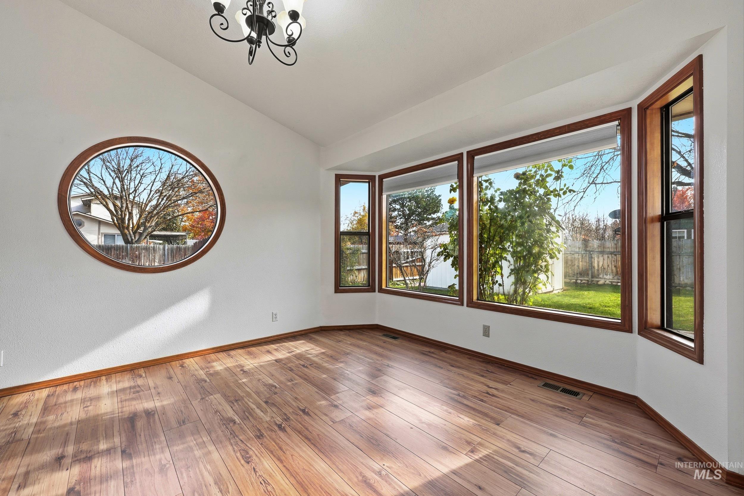 Empty room with vaulted ceiling, a chandelier, and hardwood / wood-style floors