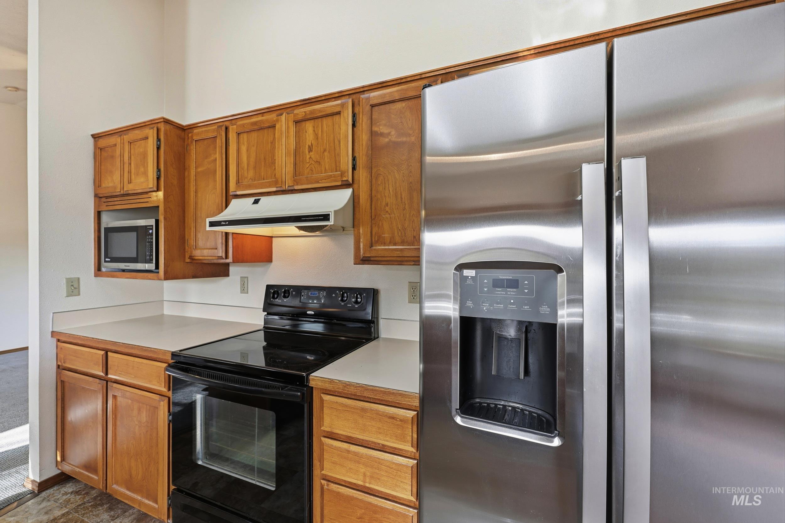 Kitchen with stainless steel appliances, light countertops, under cabinet range hood, and brown cabinets