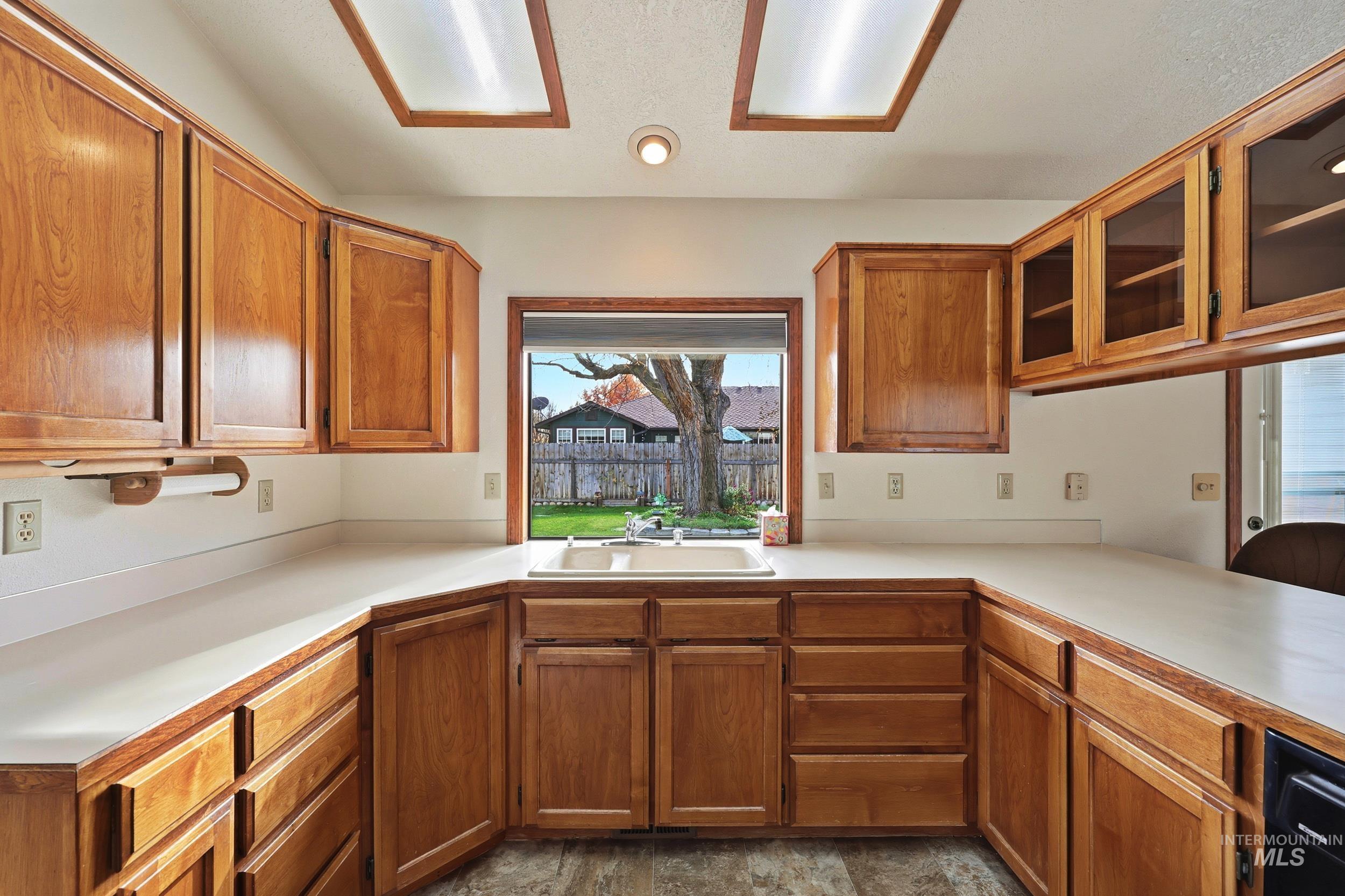 Kitchen featuring healthy amount of natural light, light countertops, glass insert cabinets, and brown cabinets