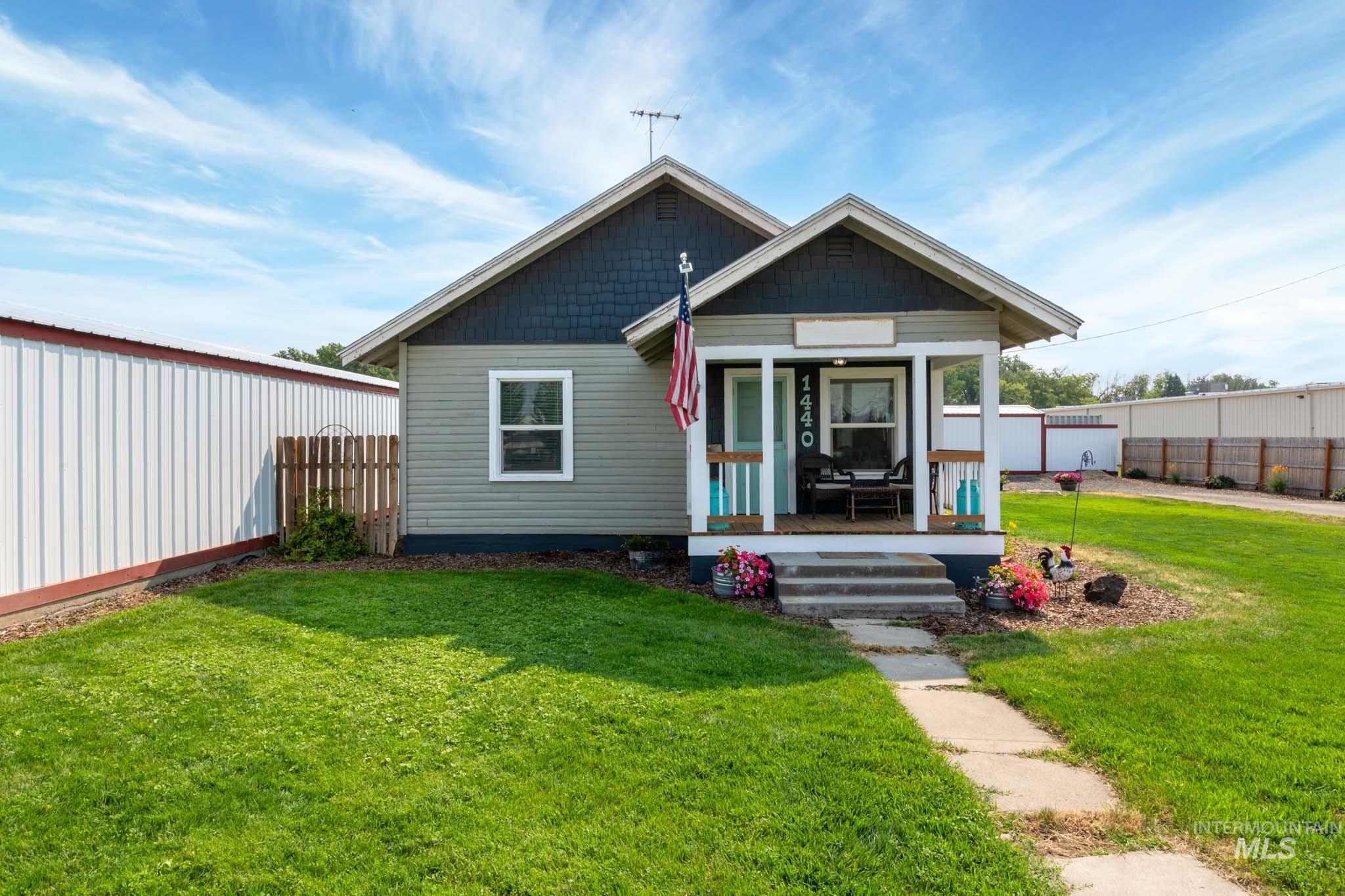 Charming exterior featuring a covered front porch, light gray siding, dark blue shingle accents, and a concrete walkway
