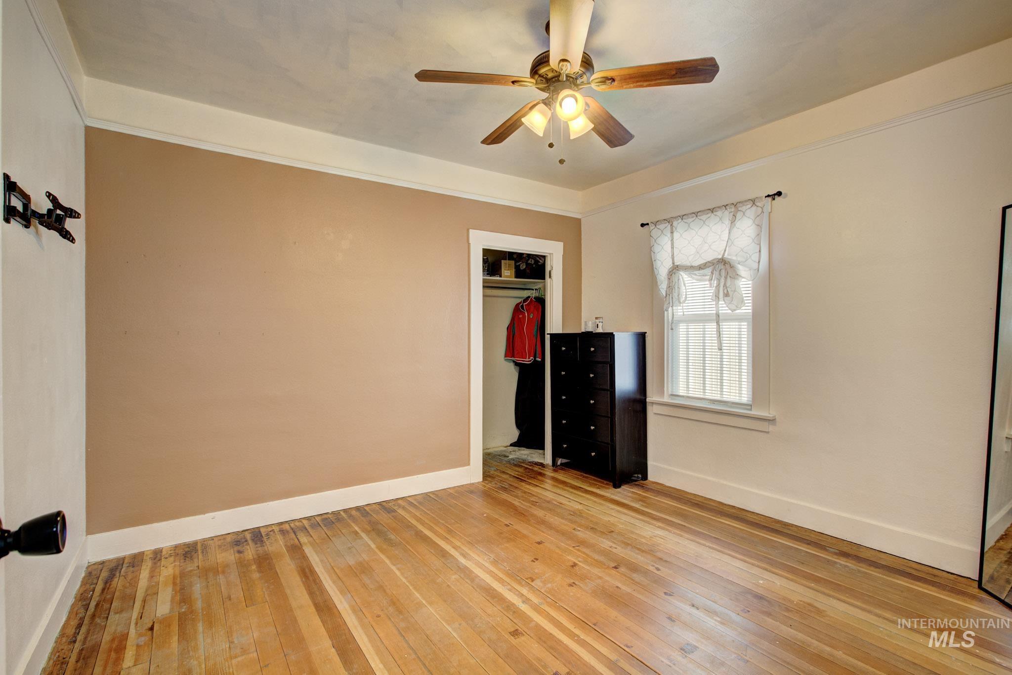 Hardwood flooring throughout featuring a ceiling fan with light fixture, a window with trim, and a built-in closet