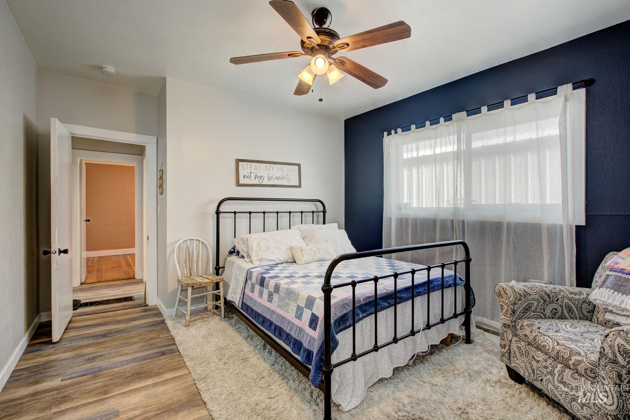 Bedroom featuring a dark accent wall, wood-finish flooring, and a ceiling fan with light fixture