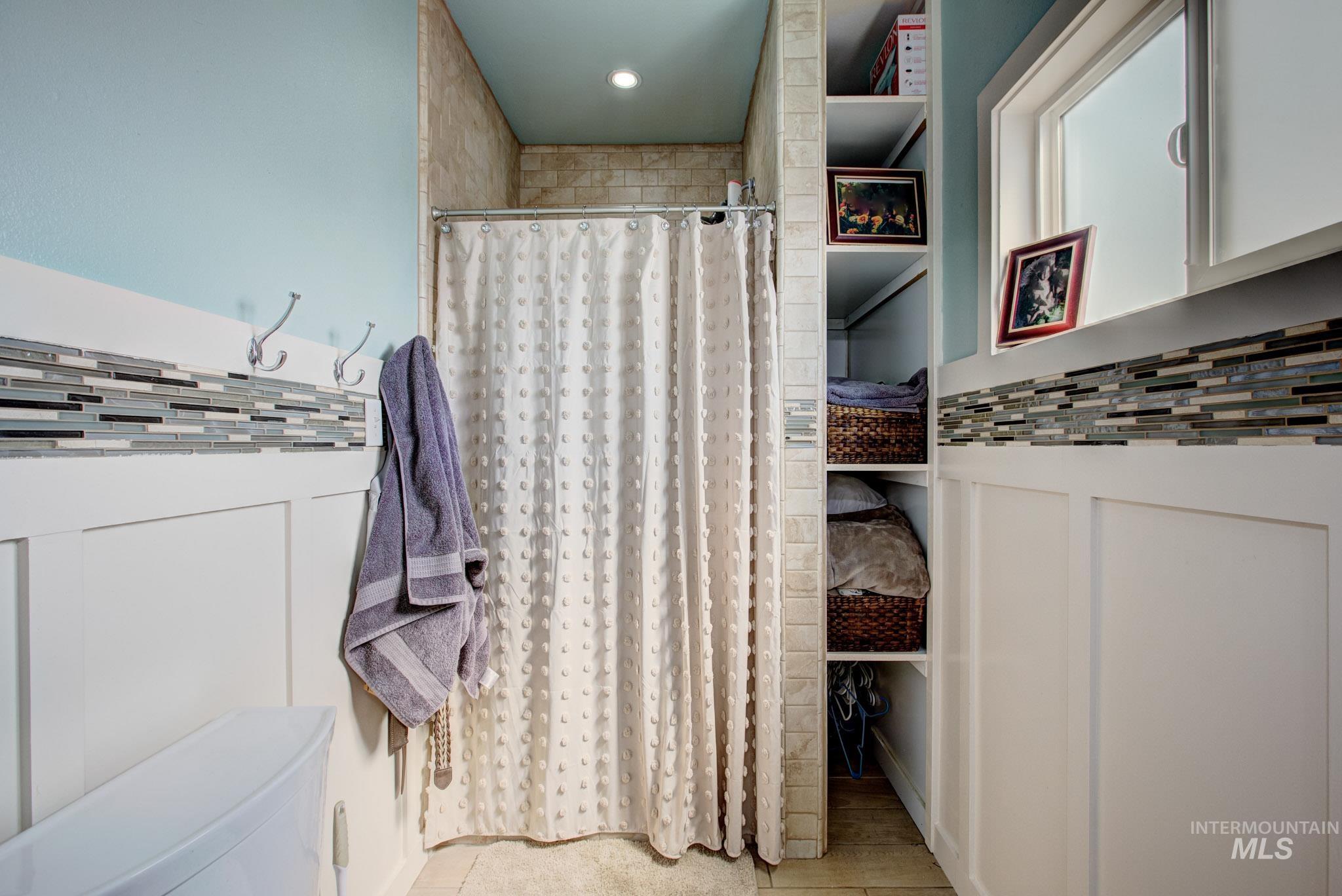 Tiled shower surround with a curtain rod, built-in shelving, white wainscoting, and a decorative tile accent band