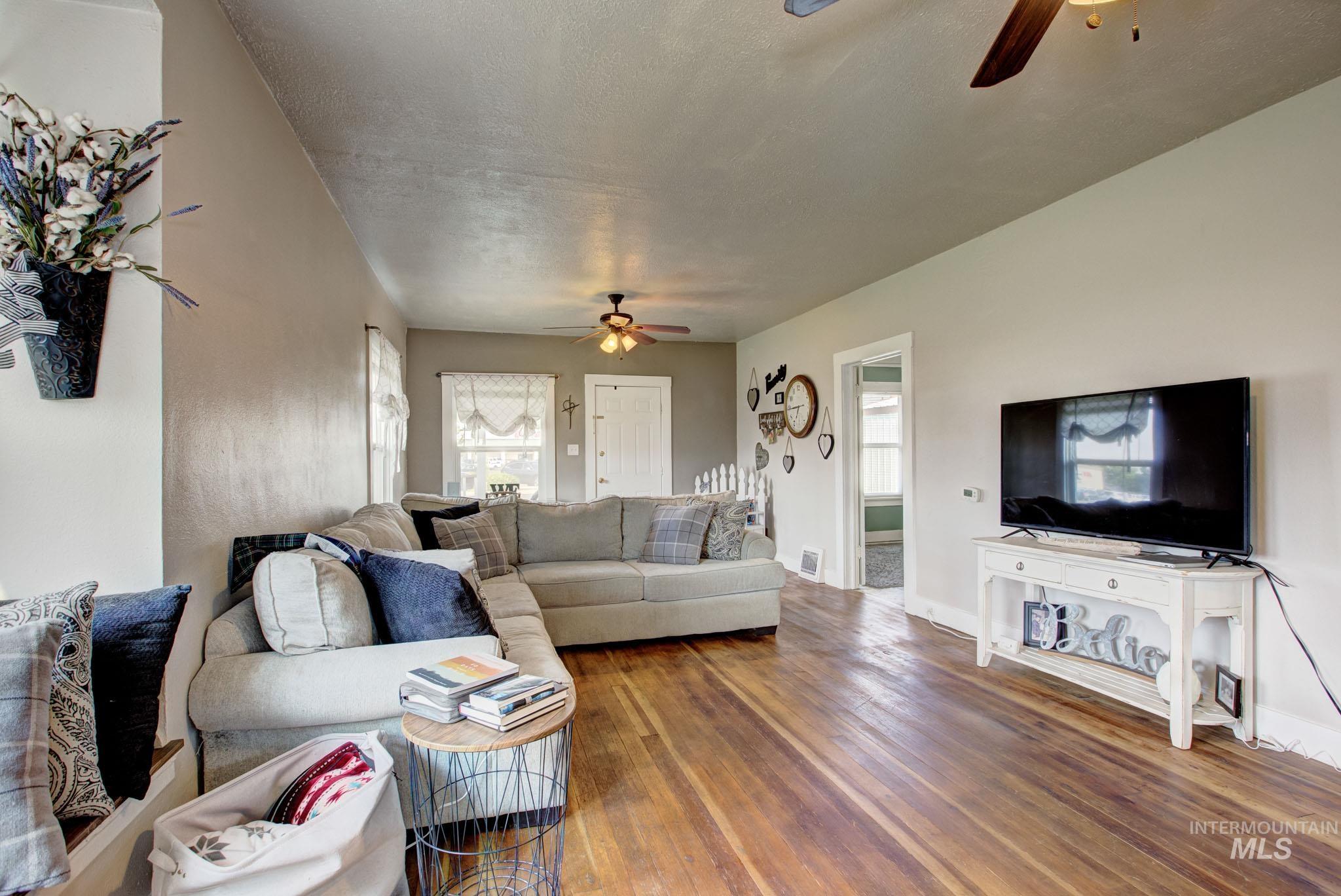 Spacious living area featuring wood-finish flooring, light neutral wall tones, and multiple windows for natural light