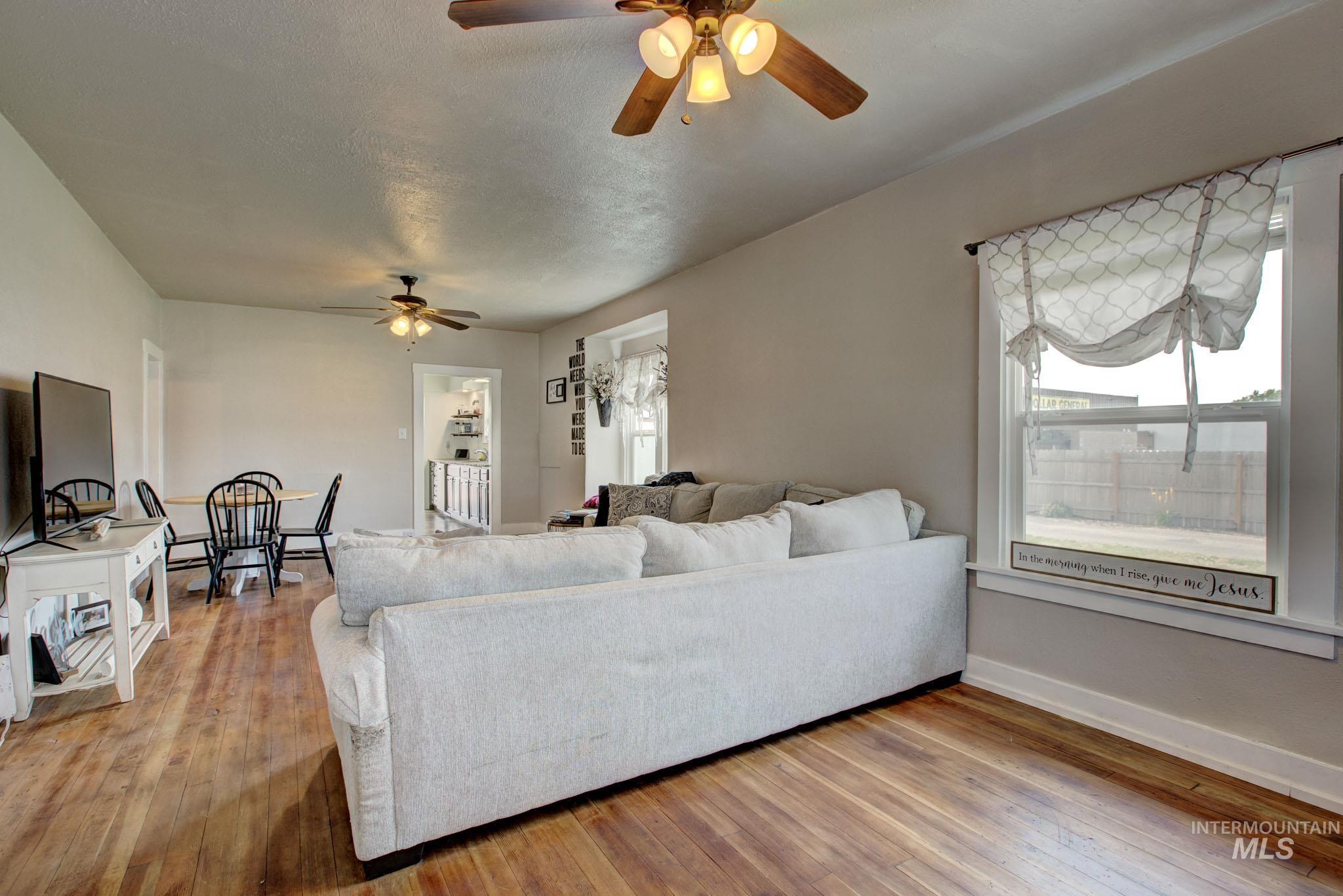 Open-concept living area featuring wood-finish flooring, neutral wall tones, and multiple ceiling fans with integrated lighting