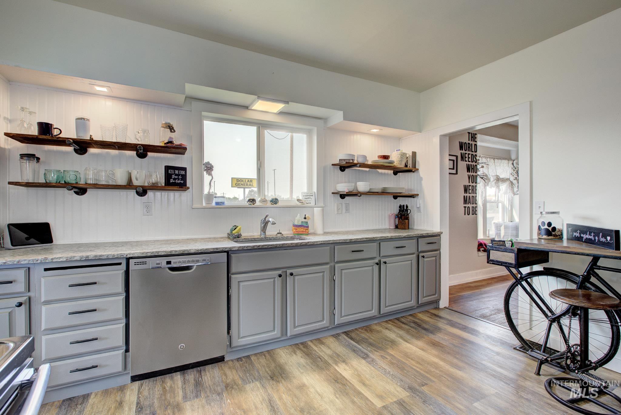 Kitchen featuring light gray cabinetry, stainless steel dishwasher, wood-finish flooring, and open shelving