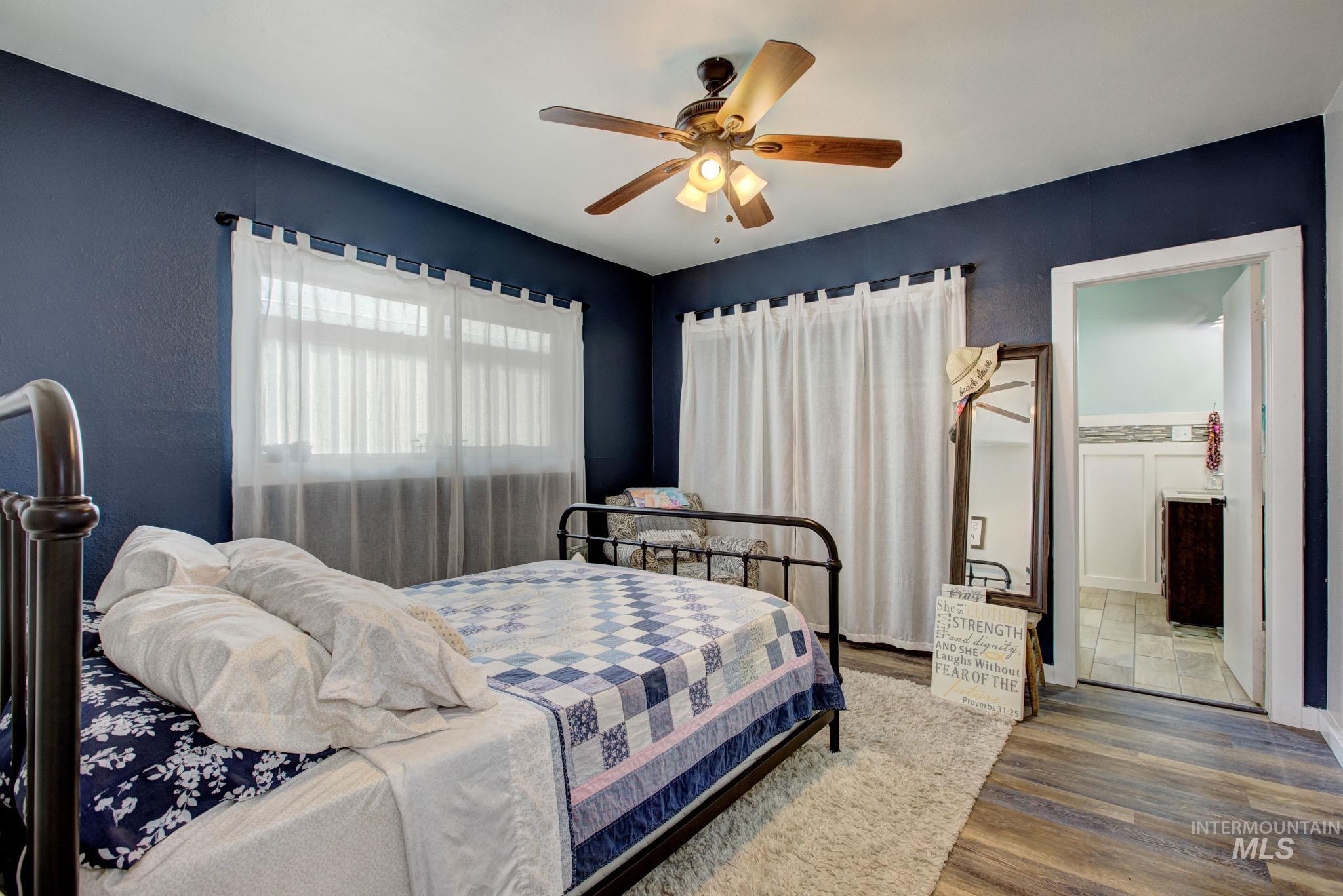 Room featuring wood-finish flooring, a ceiling fan with integrated lighting, and a window with sheer white curtains