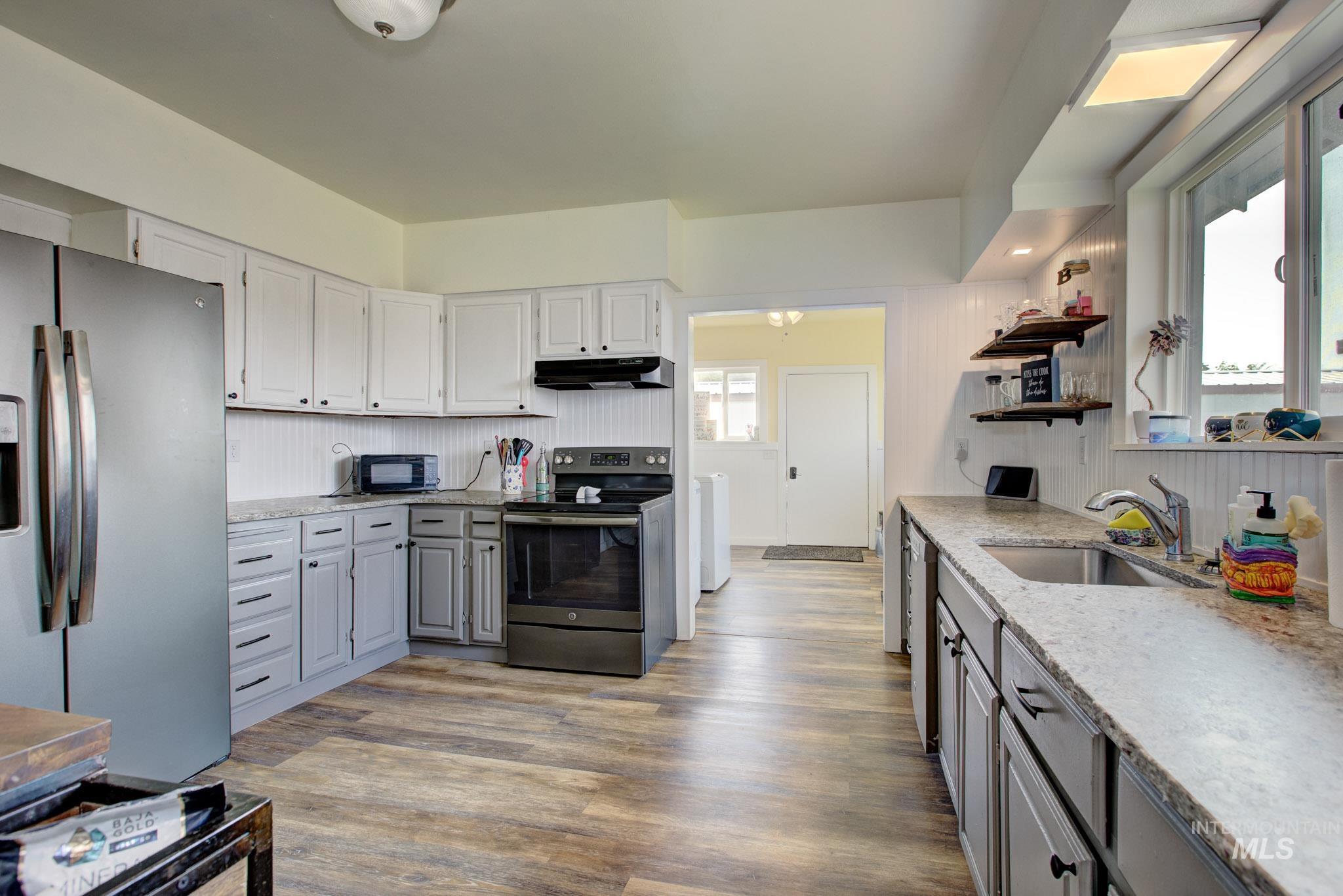 Kitchen featuring wood-finish flooring, light gray and white cabinetry, stainless steel refrigerator, black range with matching overhead microwave hood, and light-toned countertops