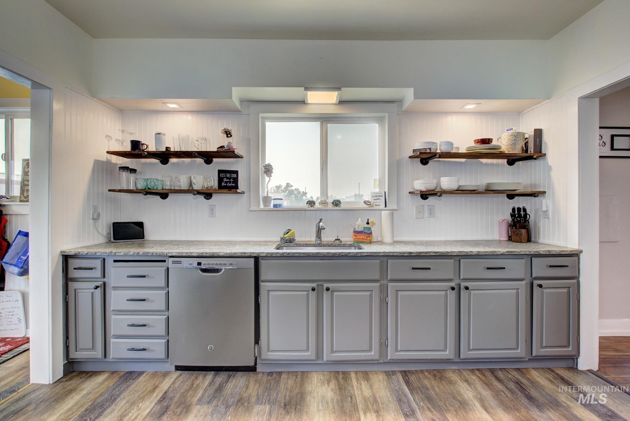 Kitchen featuring wood-finish flooring, gray lower cabinetry, a stainless steel dishwasher, and a double basin sink
