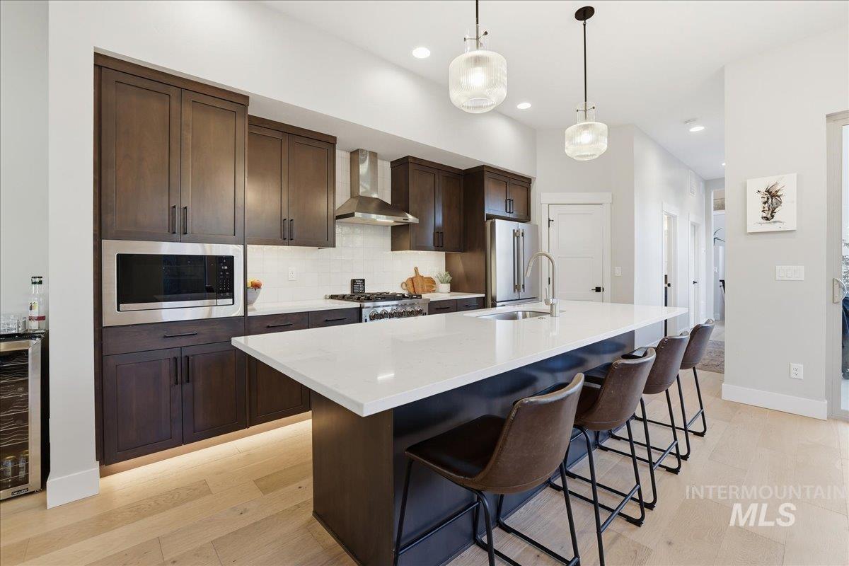 Kitchen with dark brown cabinetry, tasteful backsplash, a breakfast bar, wine cooler, and a kitchen island with sink