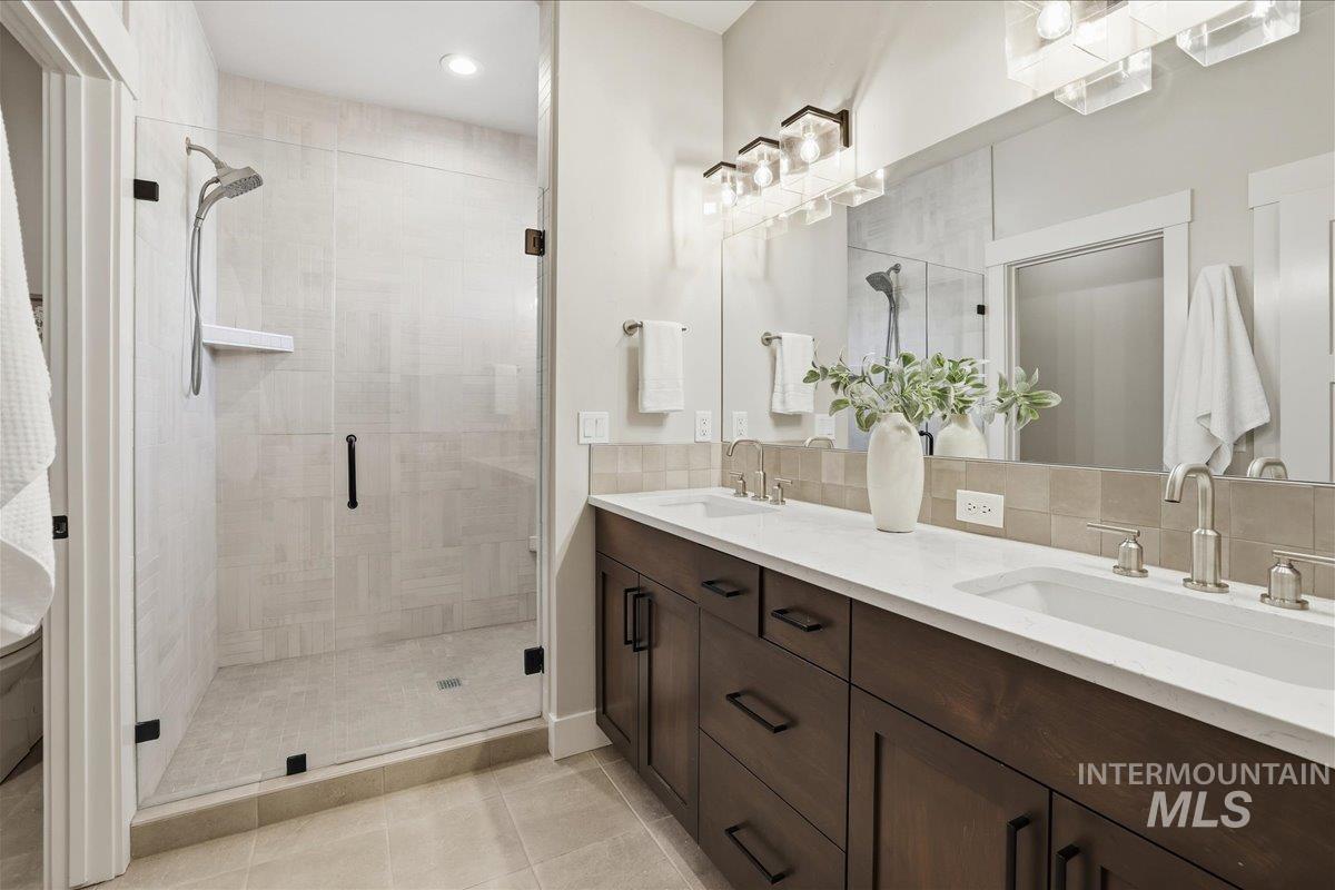 Bathroom with double vanity, a shower stall, light tile patterned floors, and decorative backsplash