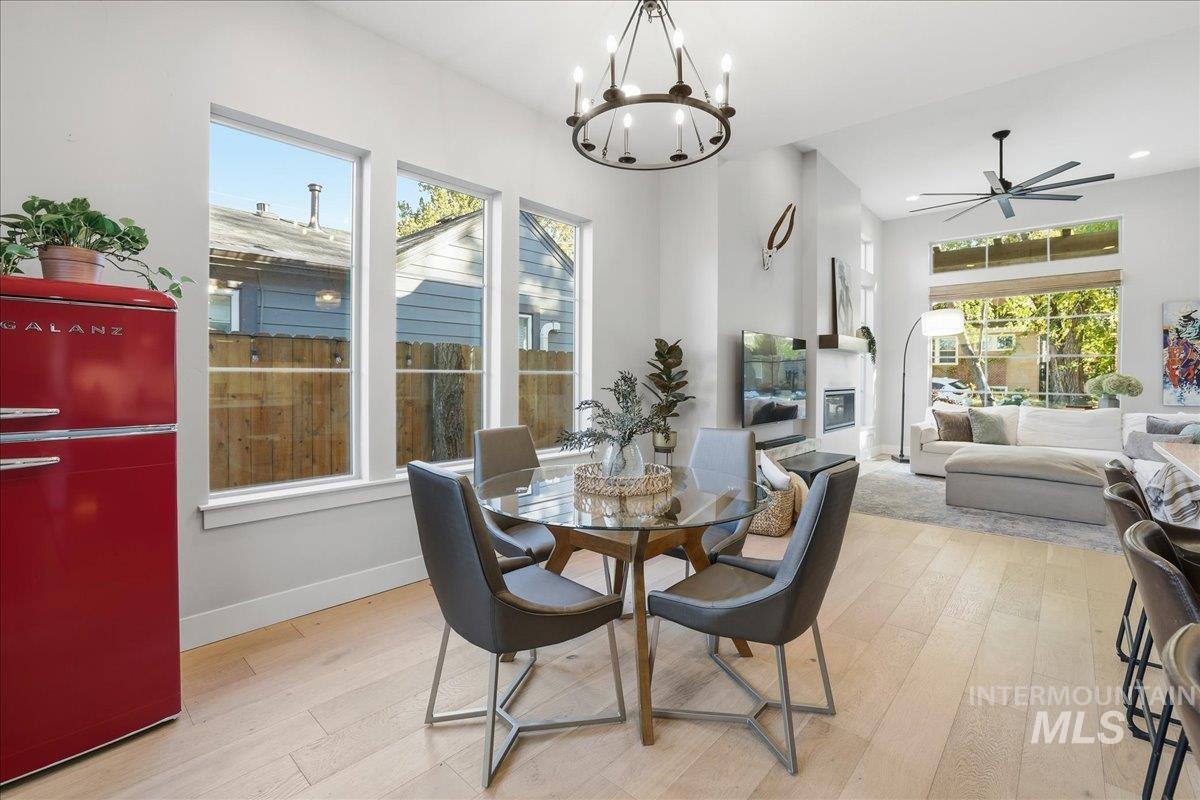 Dining space with light wood-style flooring, ceiling fan, a chandelier, and a glass covered fireplace