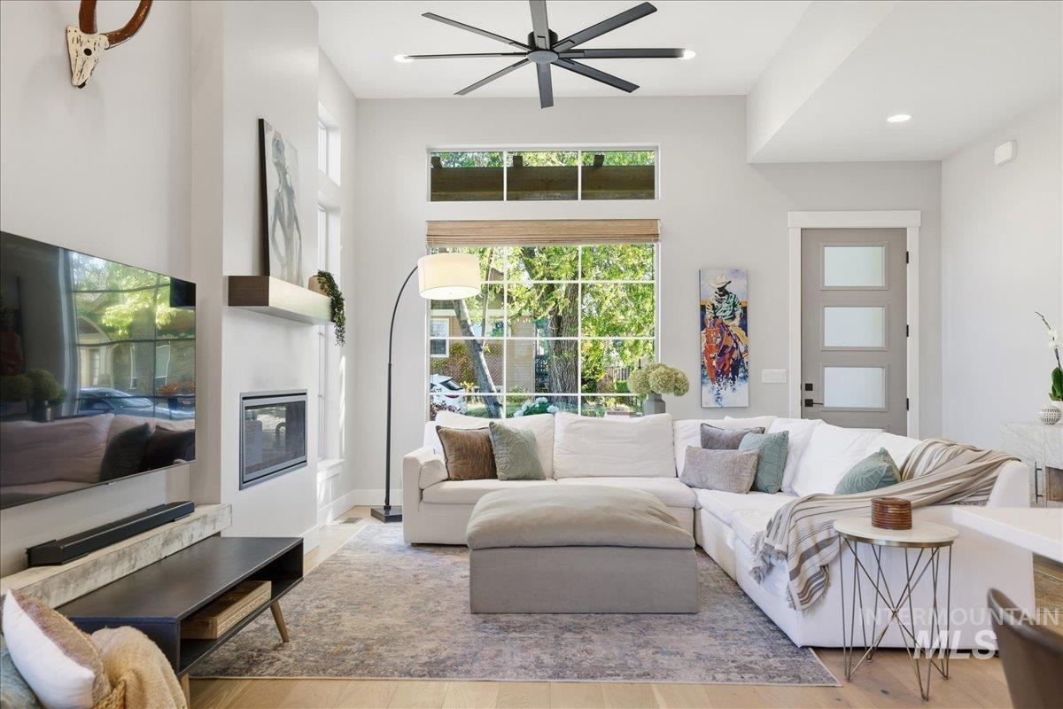 Living room with healthy amount of natural light, a glass covered fireplace, wood finished floors, ceiling fan, and recessed lighting